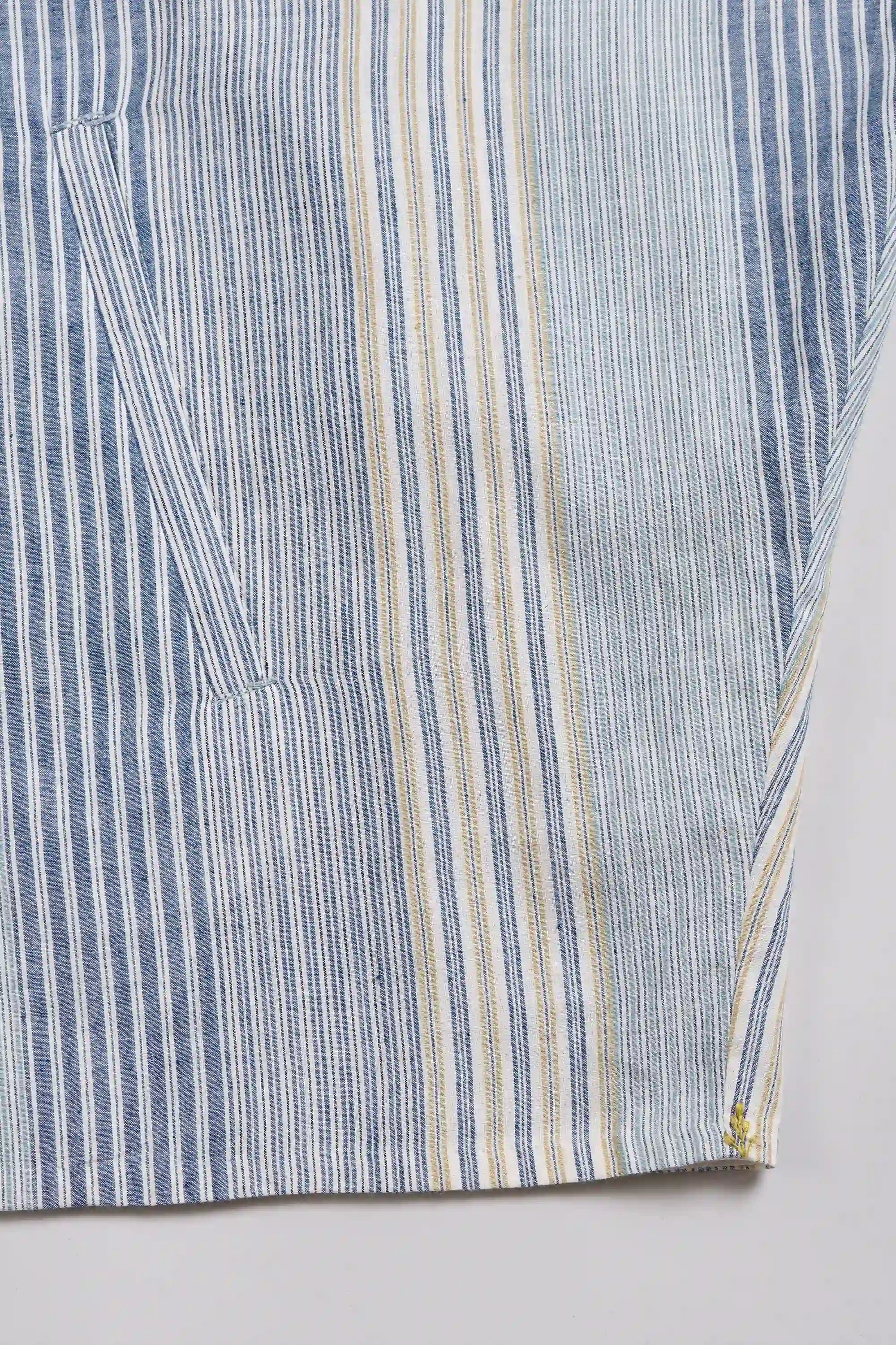 Close-up of a striped garment fabric ,white, and thin beige stripes, showing a pocket seam and hem detail
