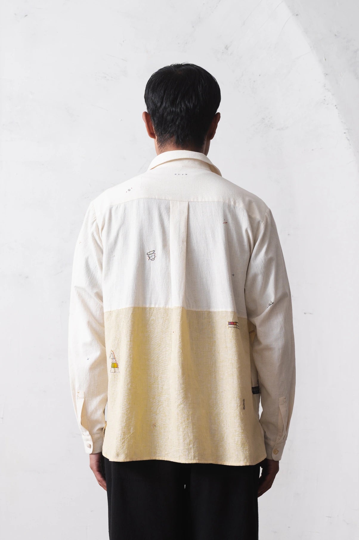 Back shot of a person wearing a shirt with hand detailing on a light grey background