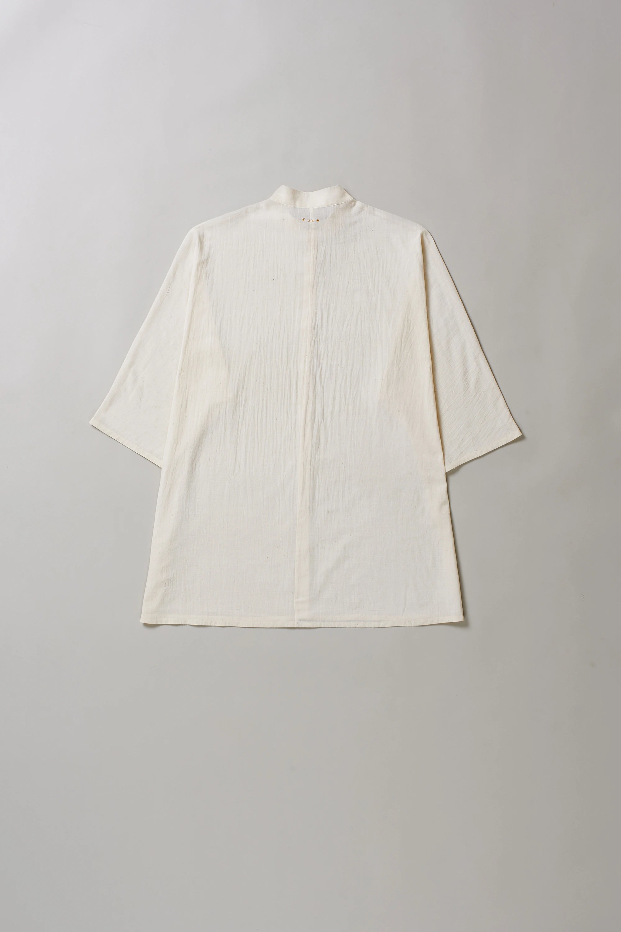 Back image of ecru cotton shirt with buttons on a grey background
