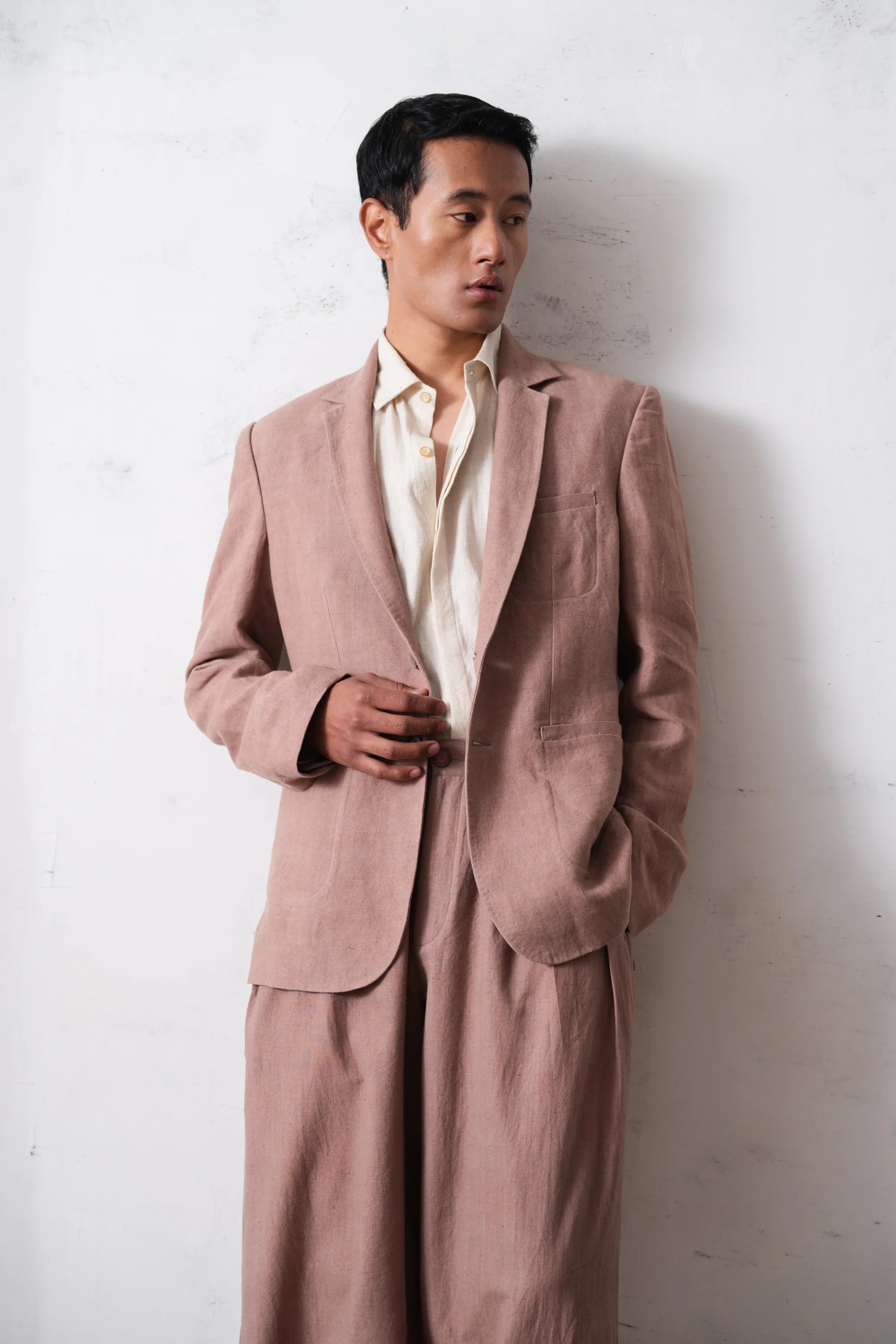 Man wearing a old rose jacket against a light grey wall