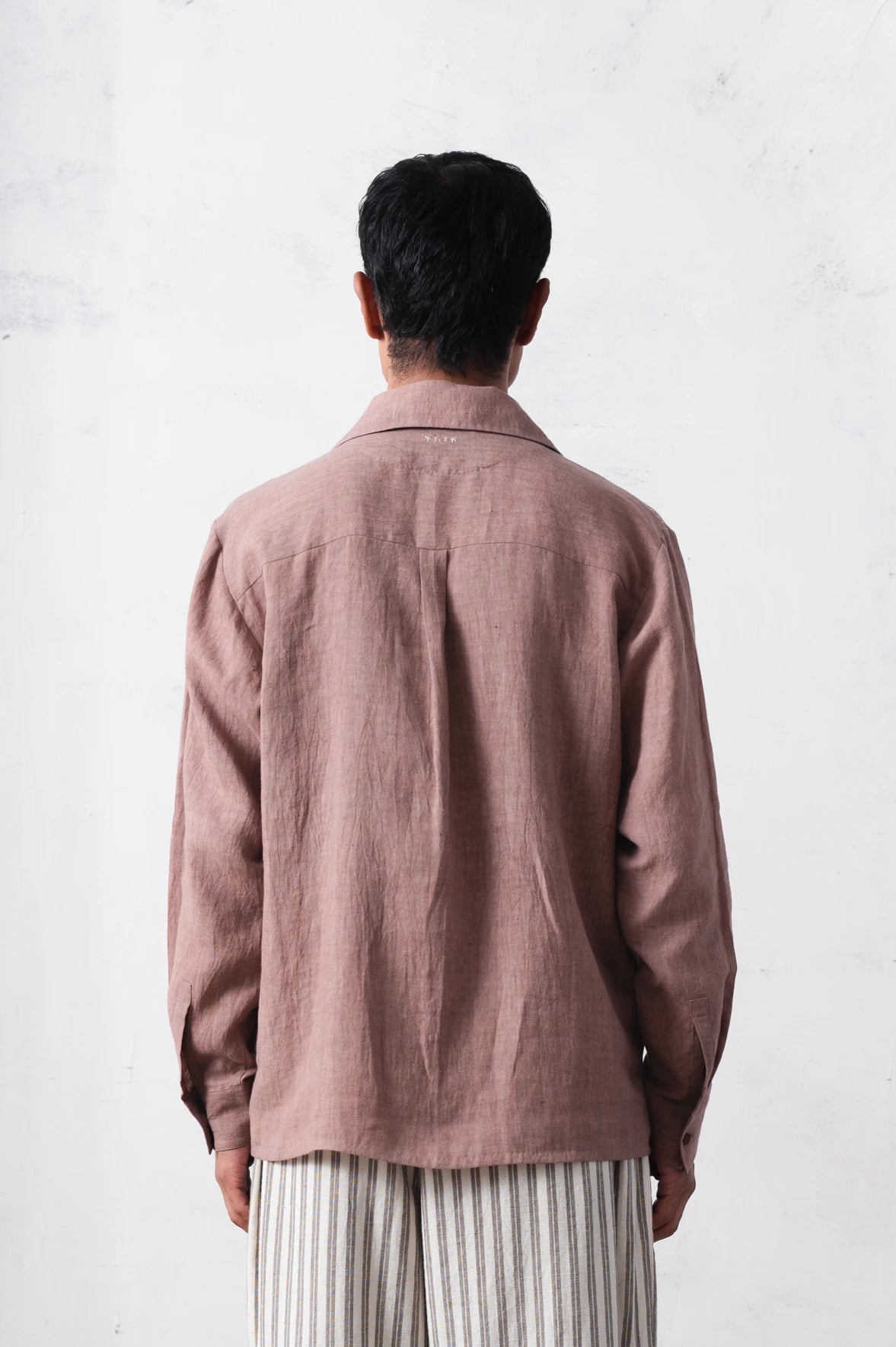 Back shot of a person wearing a shirt and striped pants against a light grey background