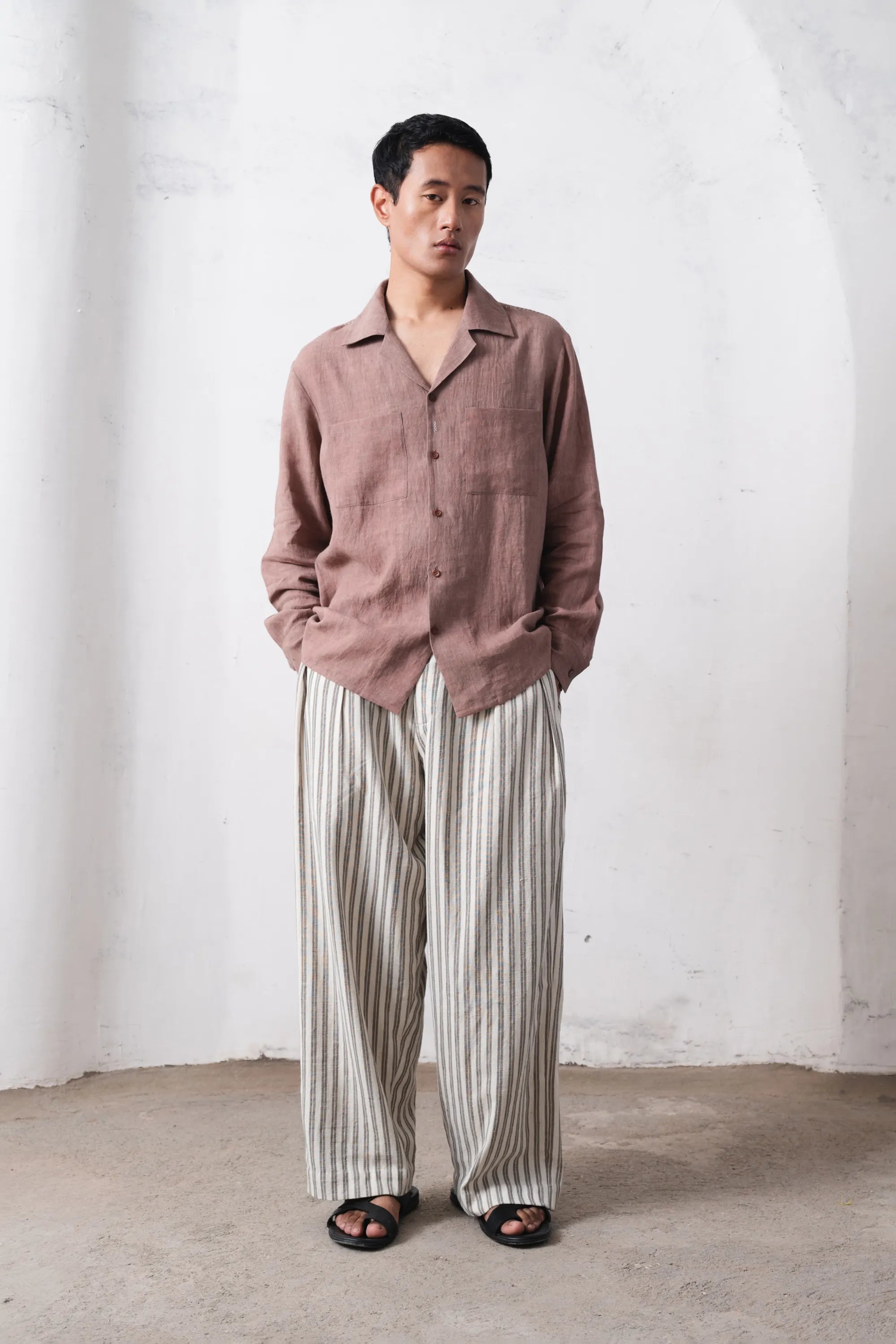 Man wearing a shirt and striped pants against a white wall