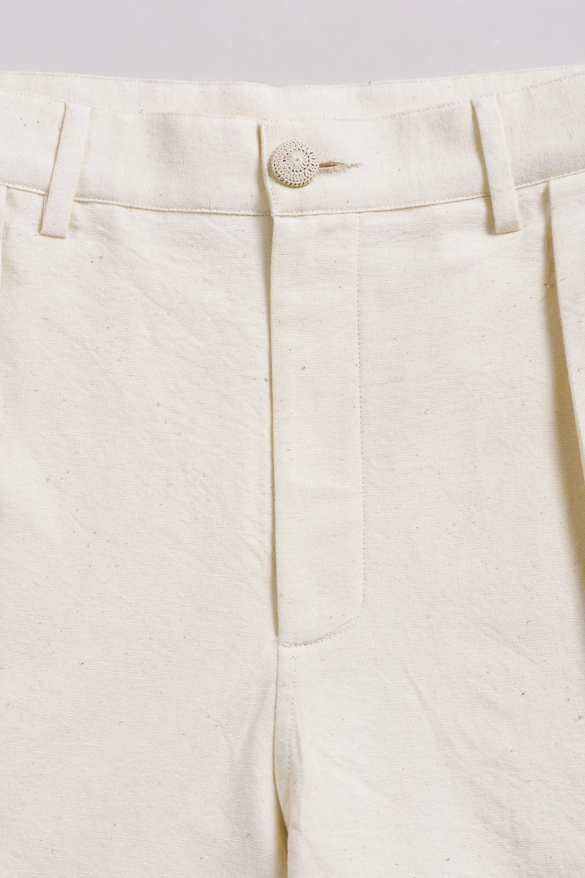 Close-up of ecru pants with a button on a light grey background