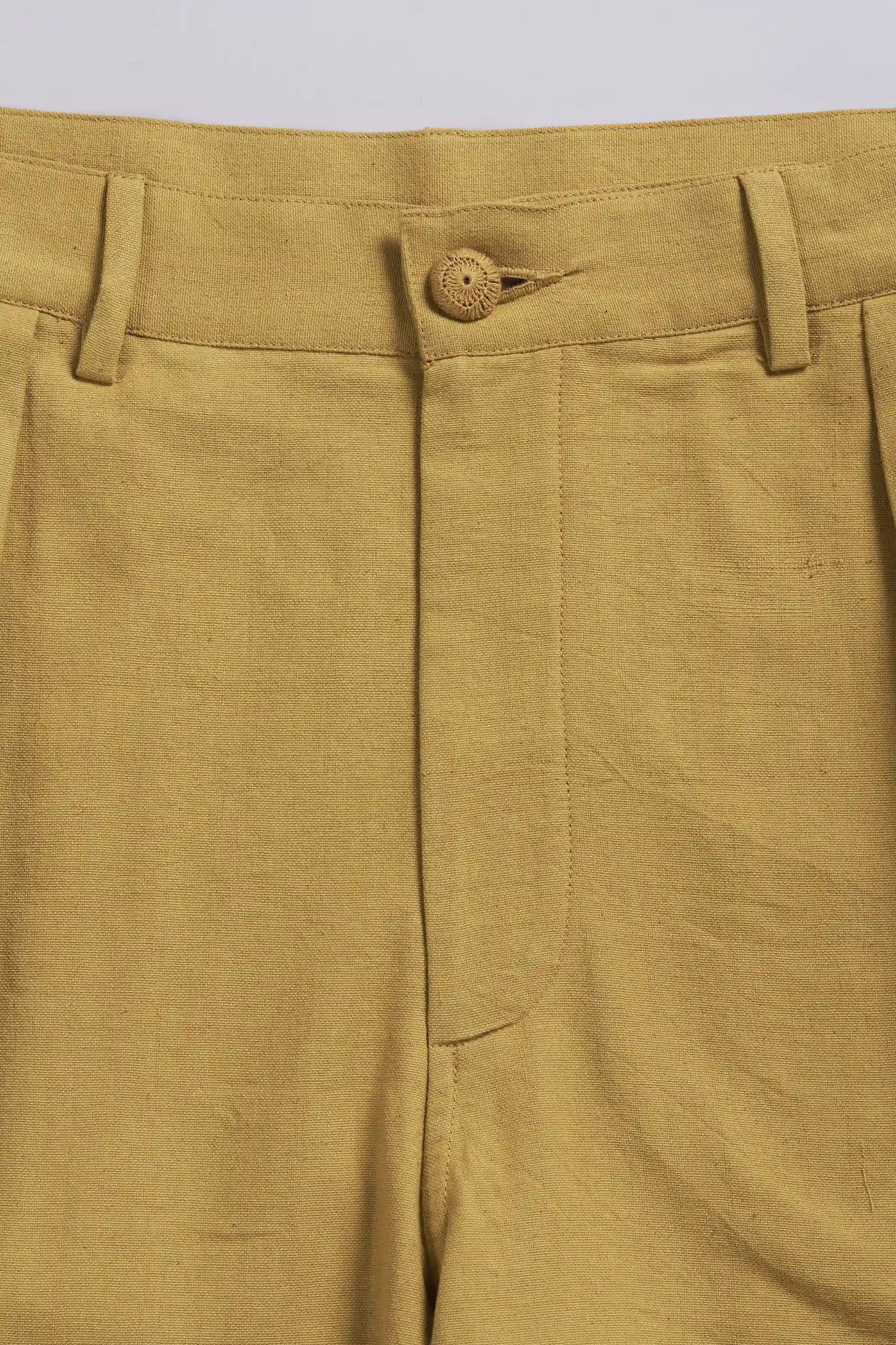 Close-up of a ochre yellow pleated shorts with a button on a light grey background