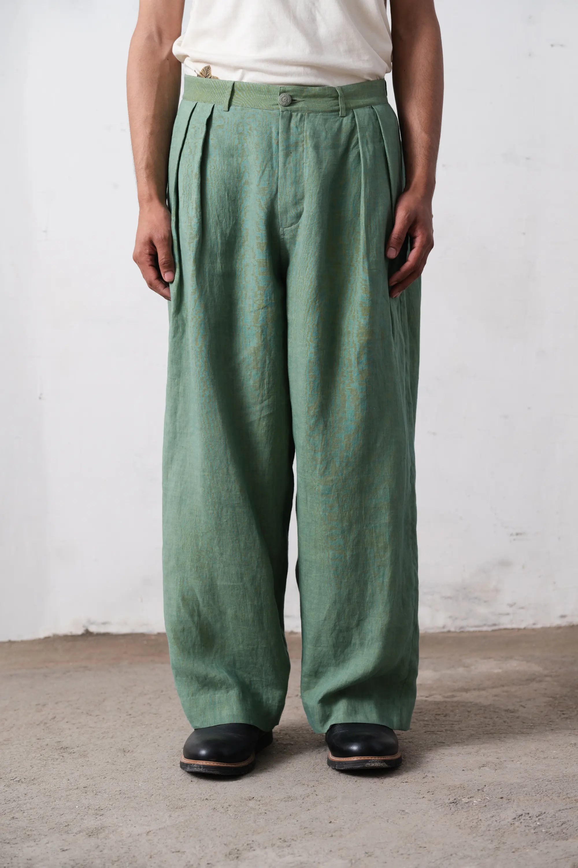 Person wearing green pleated pants against a light grey wall