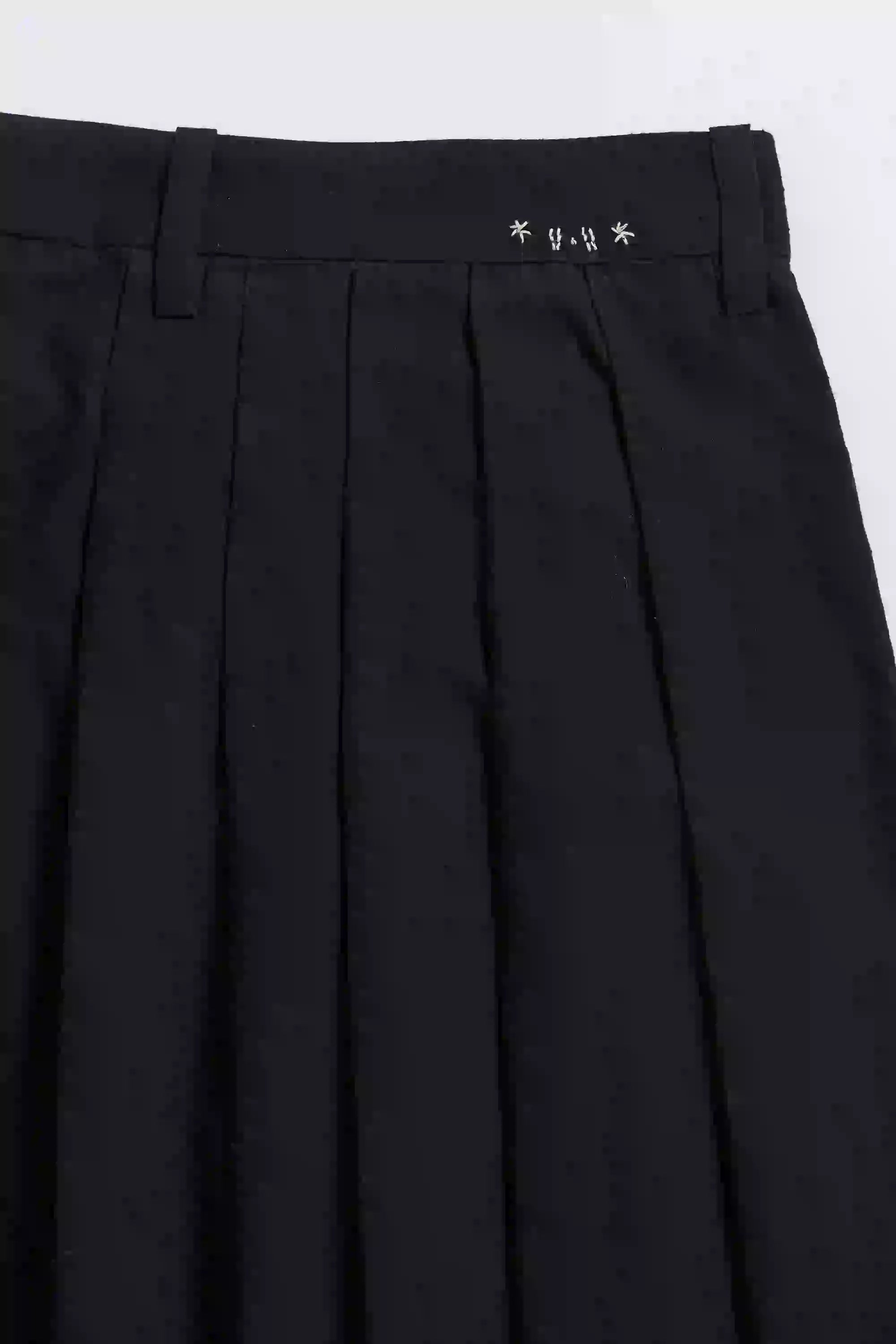 Black pleated pants with a brand logo on the waistband against a white background