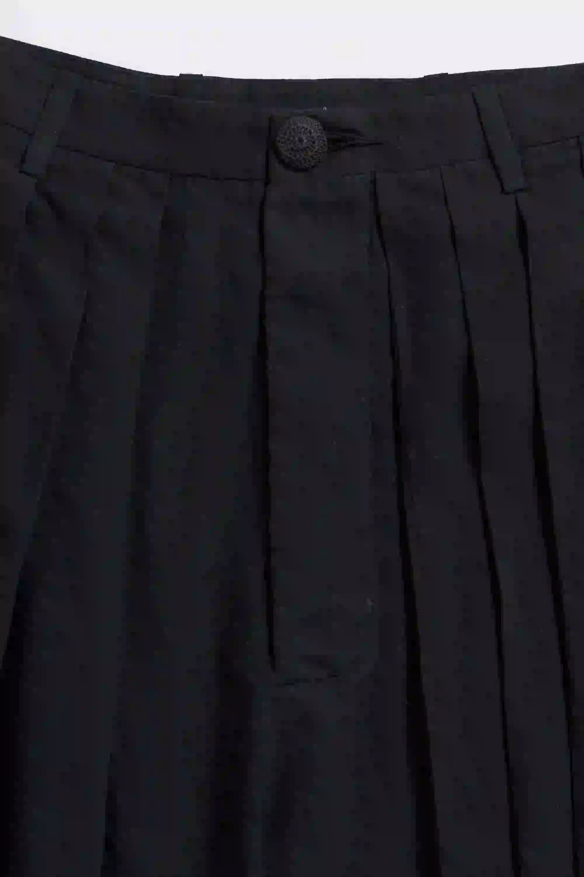 Close-up of black pleated pants with a button on a white background