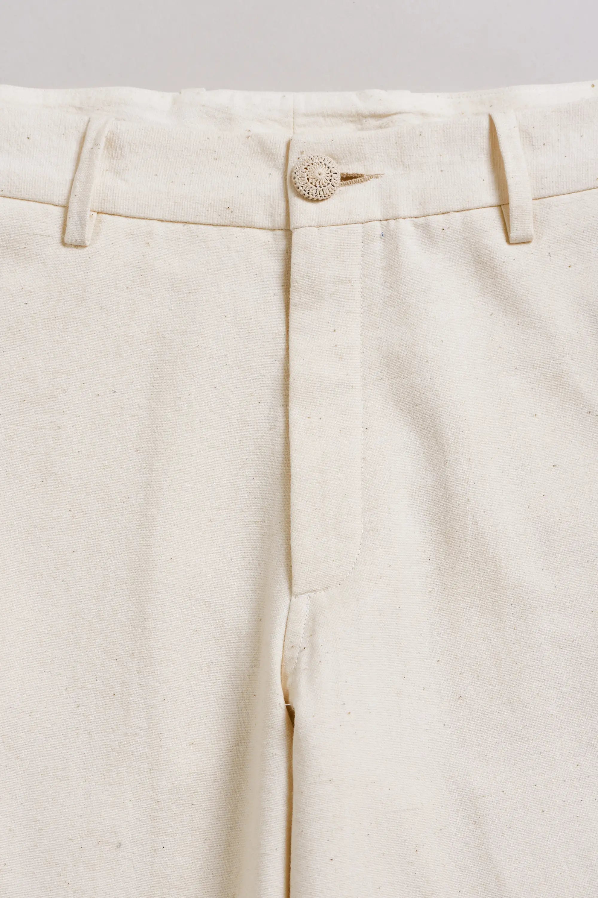 Close-up of ecru pants with a button on a light grey background