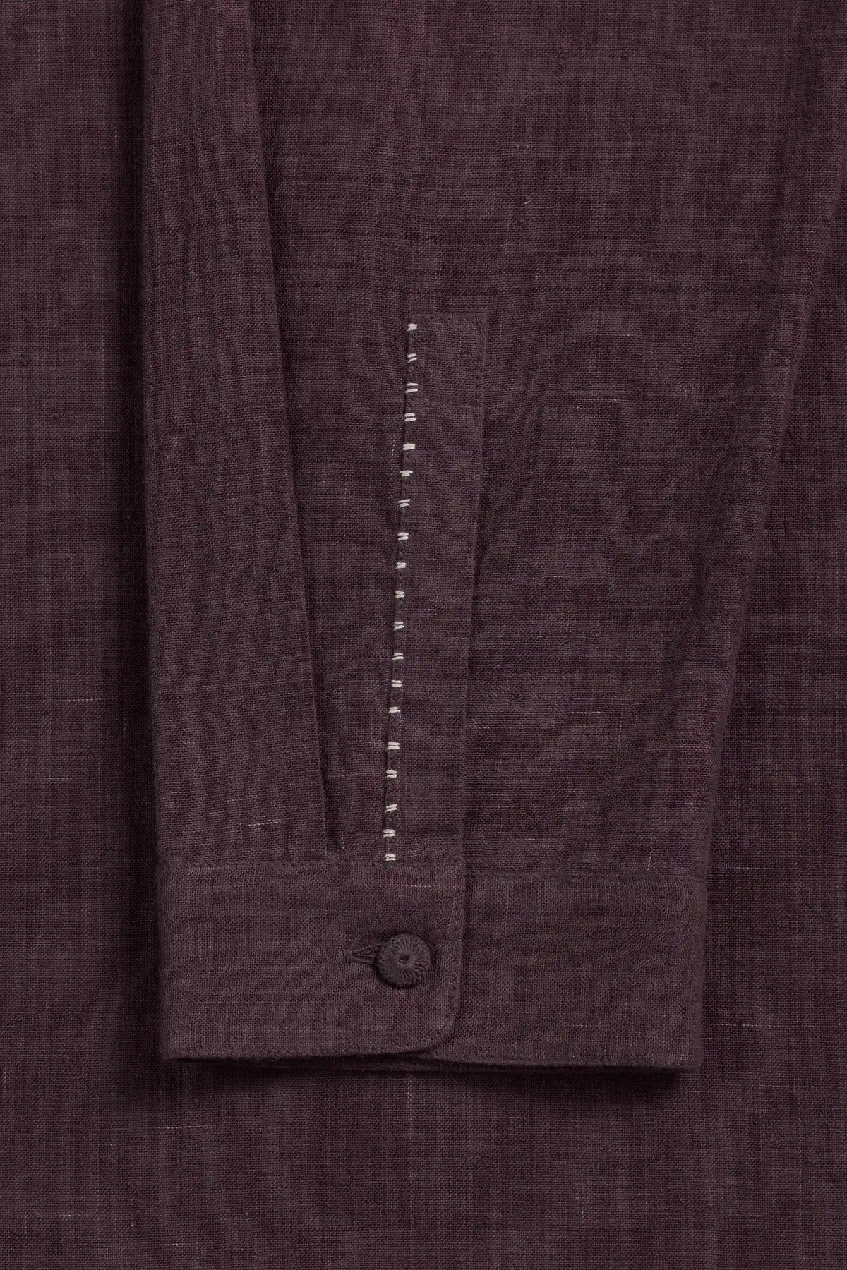 Close-up of purple red colored textured fabric garment, showing a buttoned cuff with a vertical row of white contrast stitching.