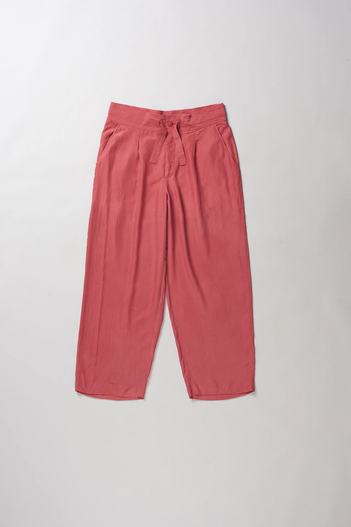 A pair of relaxed-fit, wide-leg pants in a dusty rose or muted coral pink color, laid flat against a light grey background.