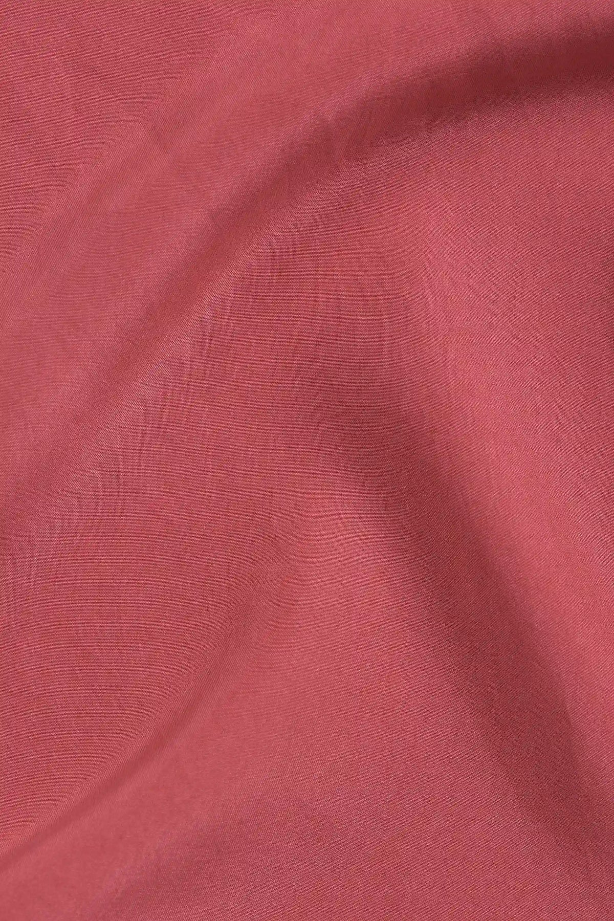 A close-up of draped dusty rose pink fabric with soft folds and a smooth texture.