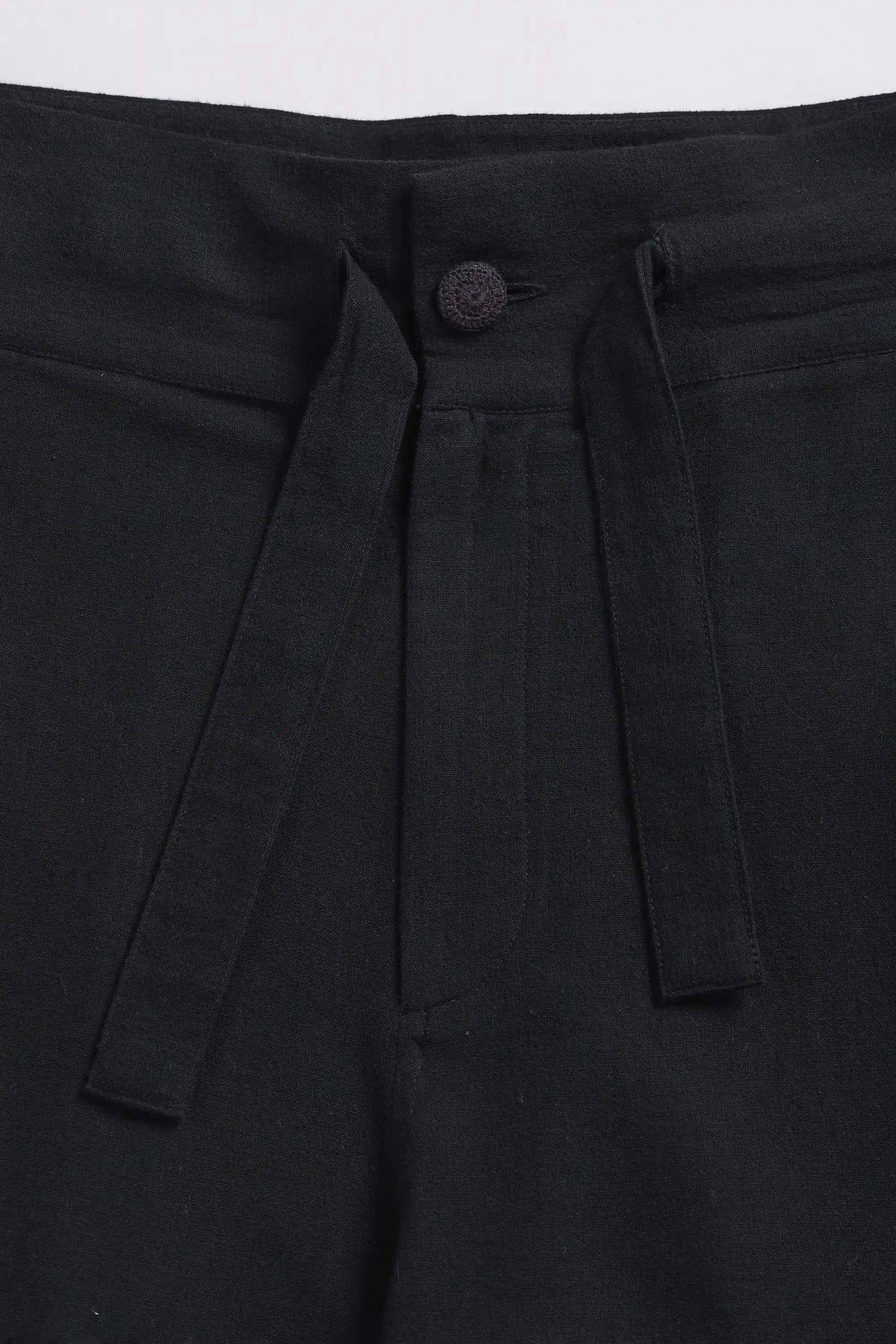 Close-up of black pants with a button and belt loops on a light grey background