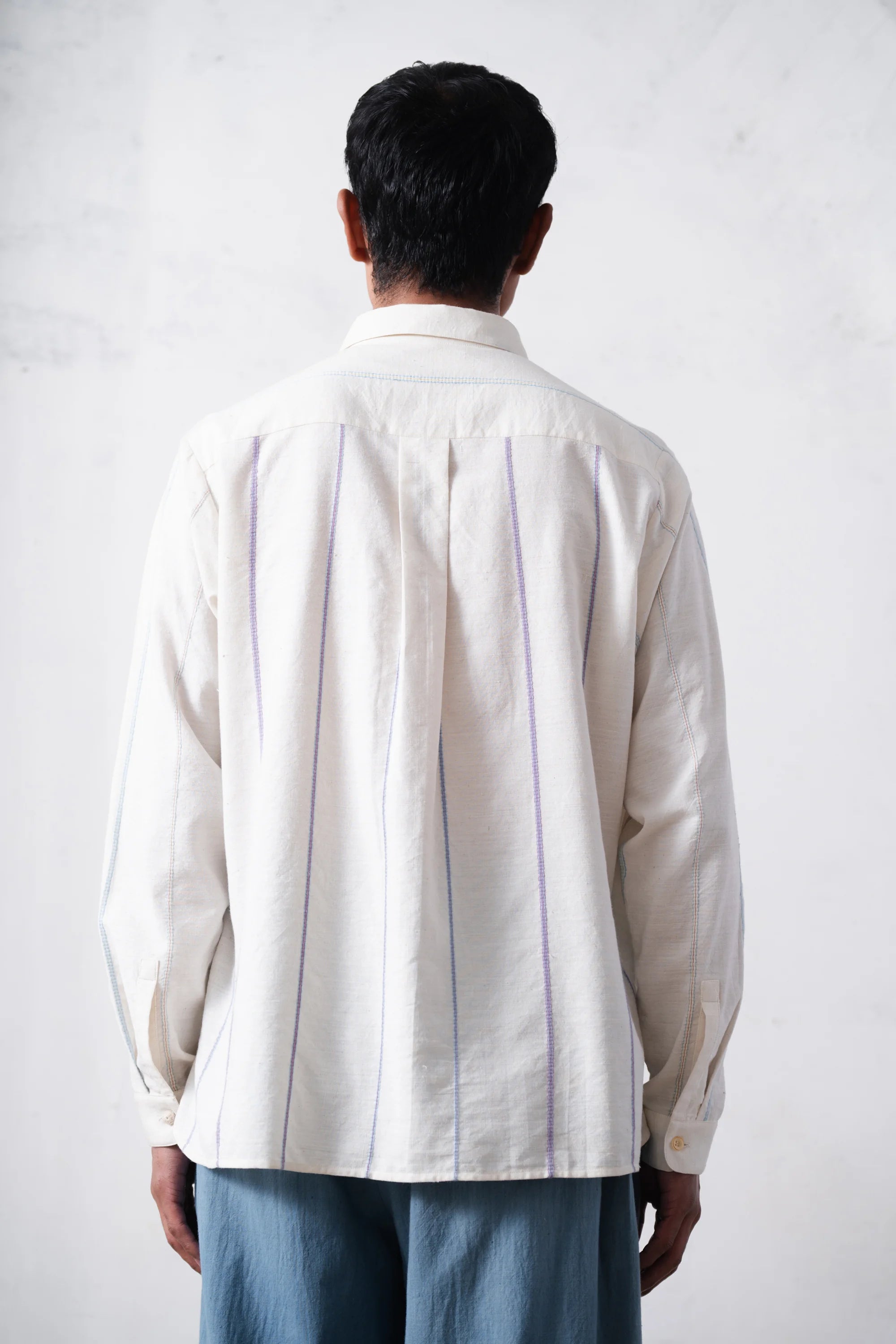 Back shot of a person wearing a ecru shirt with pleated details on a light grey background