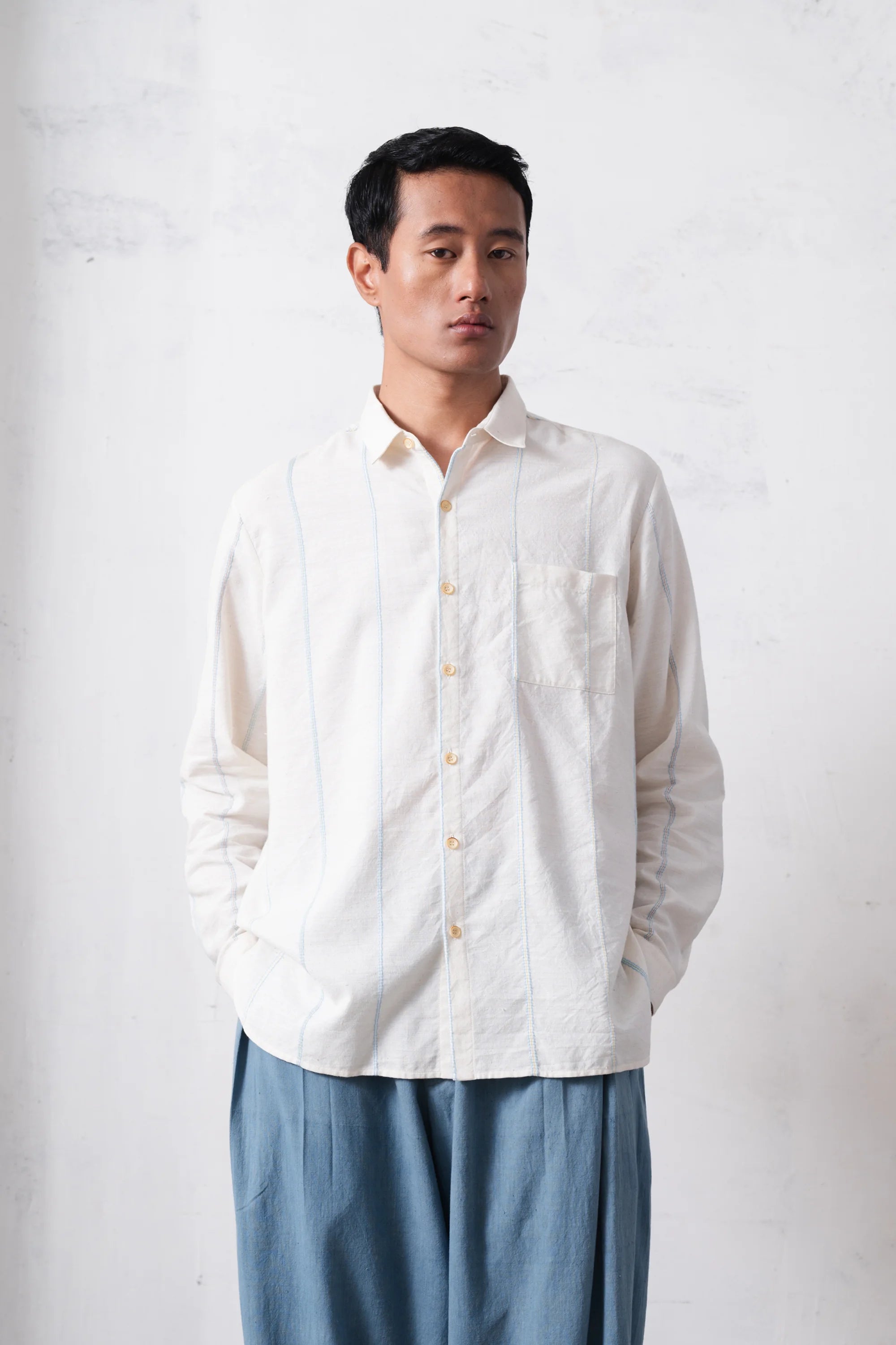 Man wearing a white shirt and blue pants against a light grey background