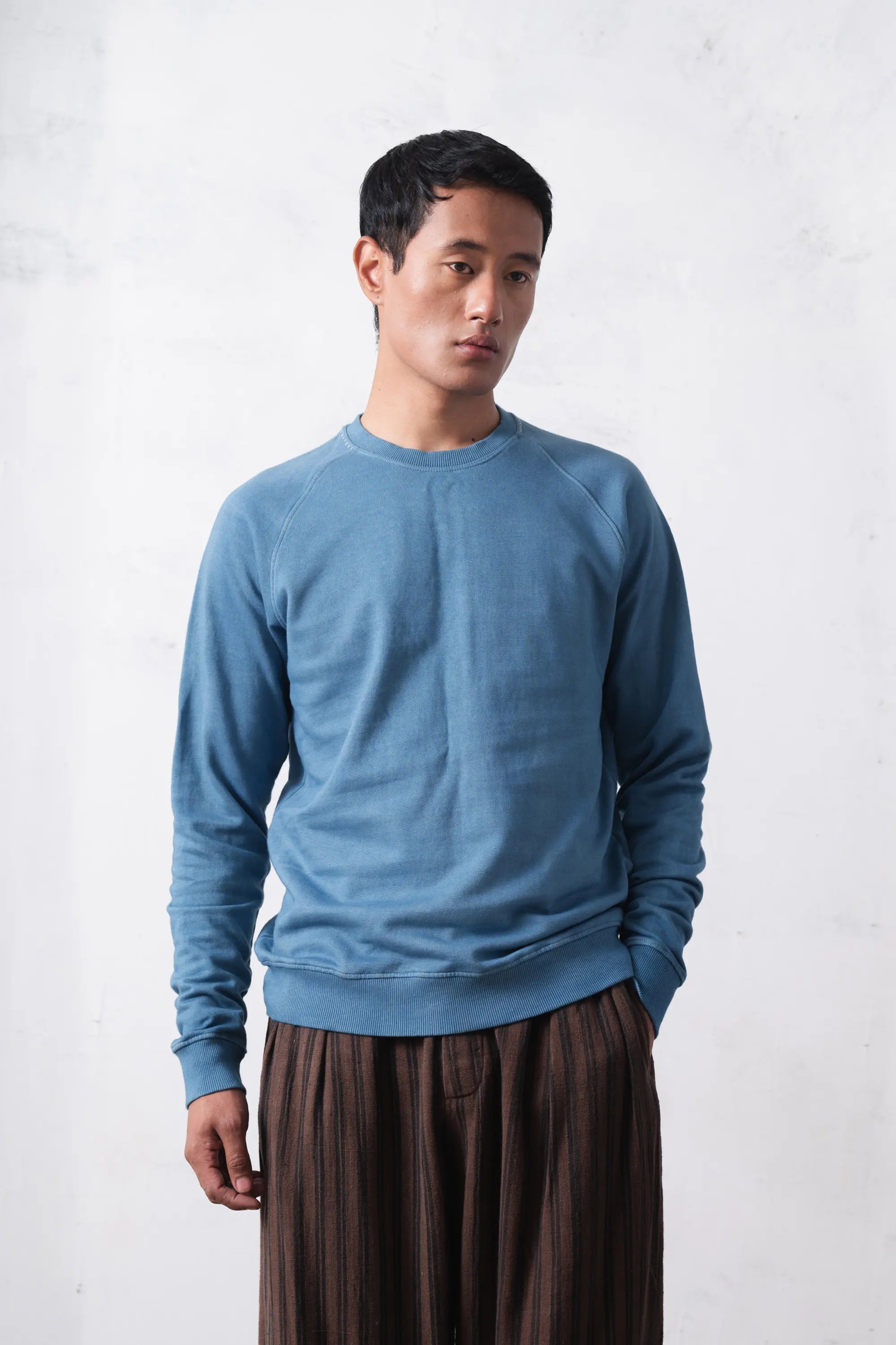 Man wearing a blue sweater and brown pants against a light grey background