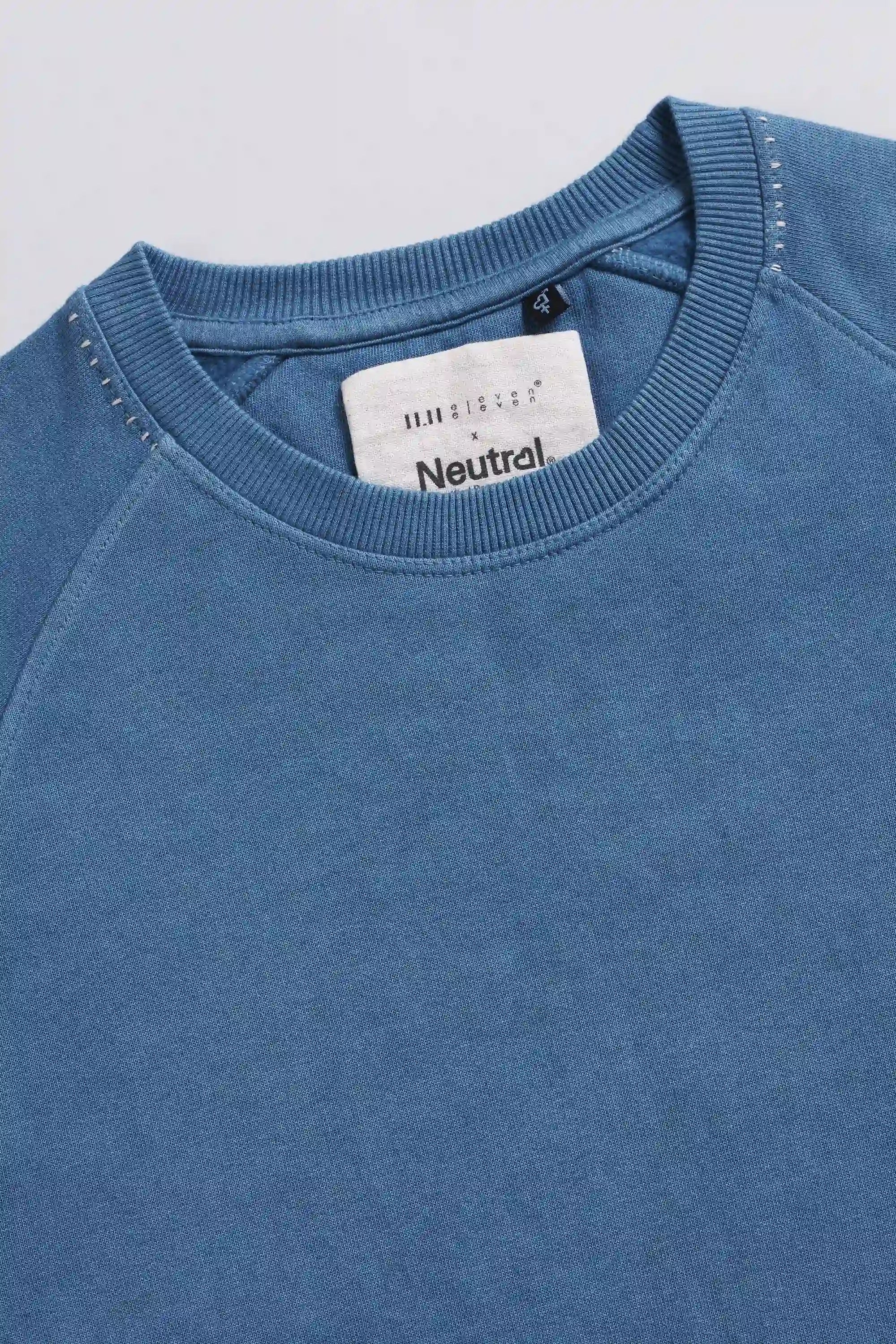 Close-up of a blue sweatshirt with a brand label on a light grey background