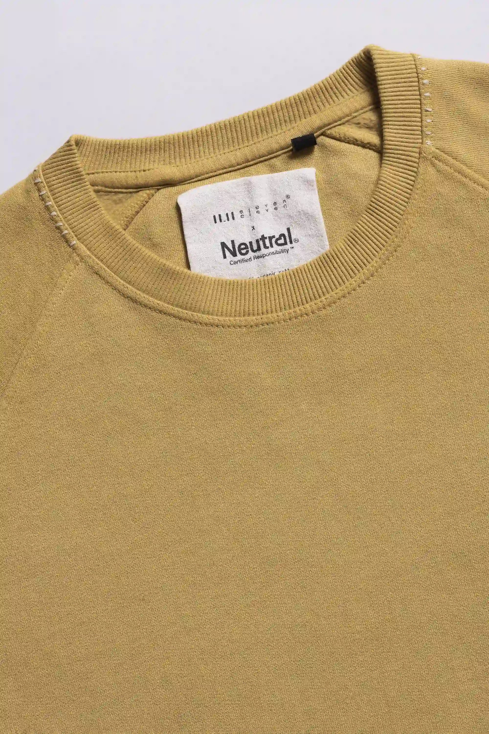 Close-up of a ochre yellow sweatshirt with a brand label on a light grey background
