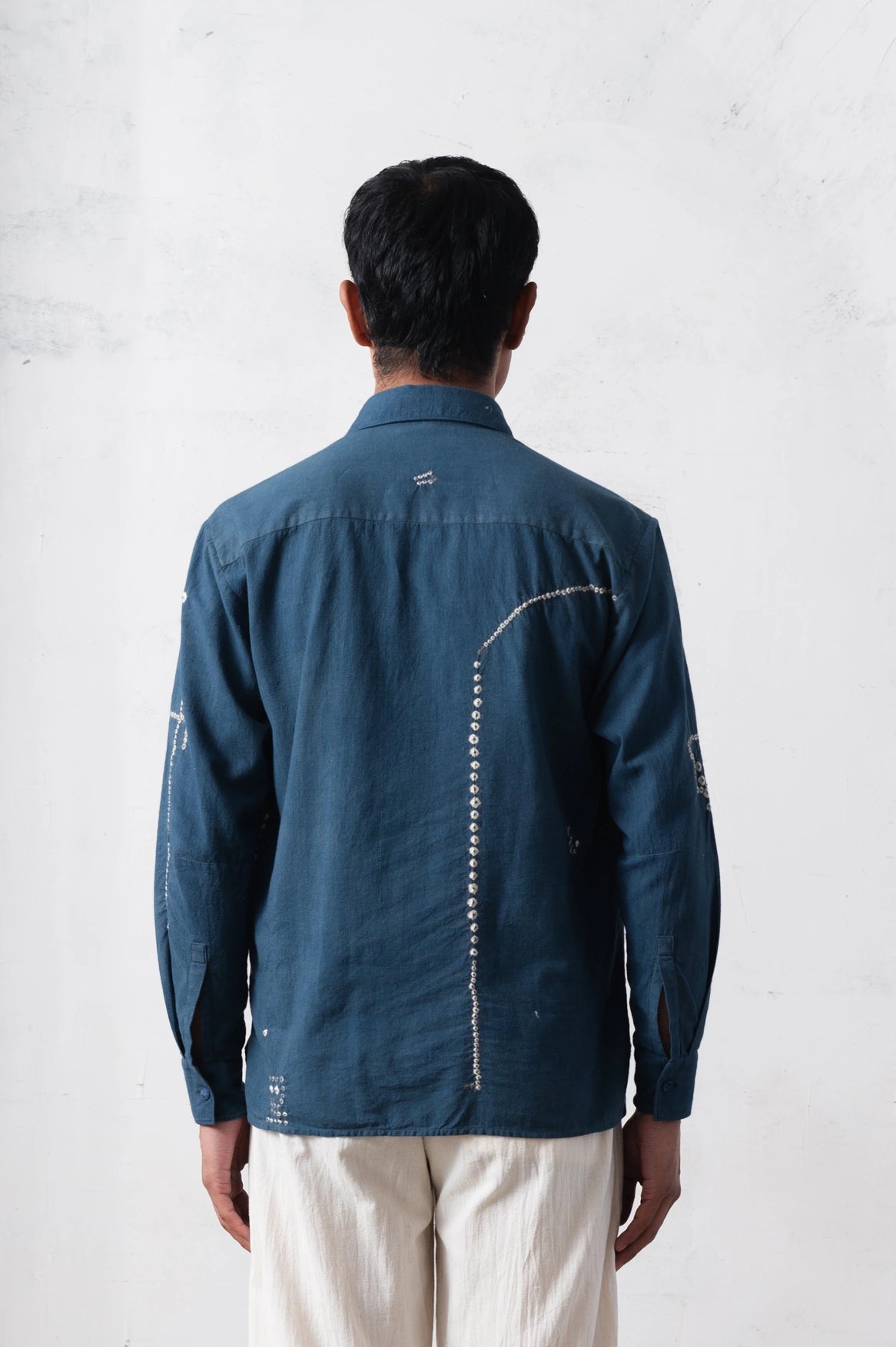 Person wearing a dark blue shirt with hand shibori work on a light grey background