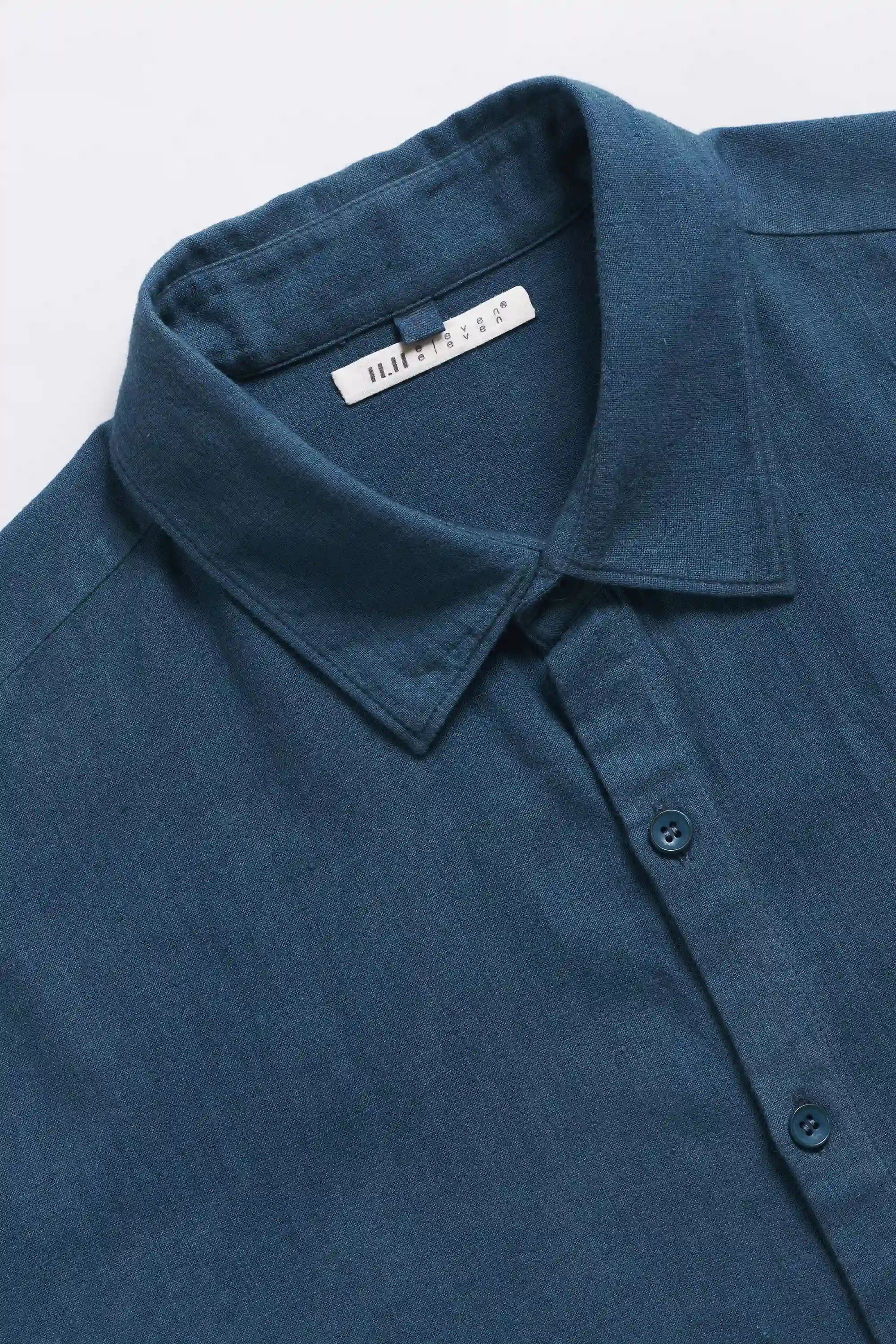 Close-up of a blue shirt collar with a brand label and buttons on a light grey background