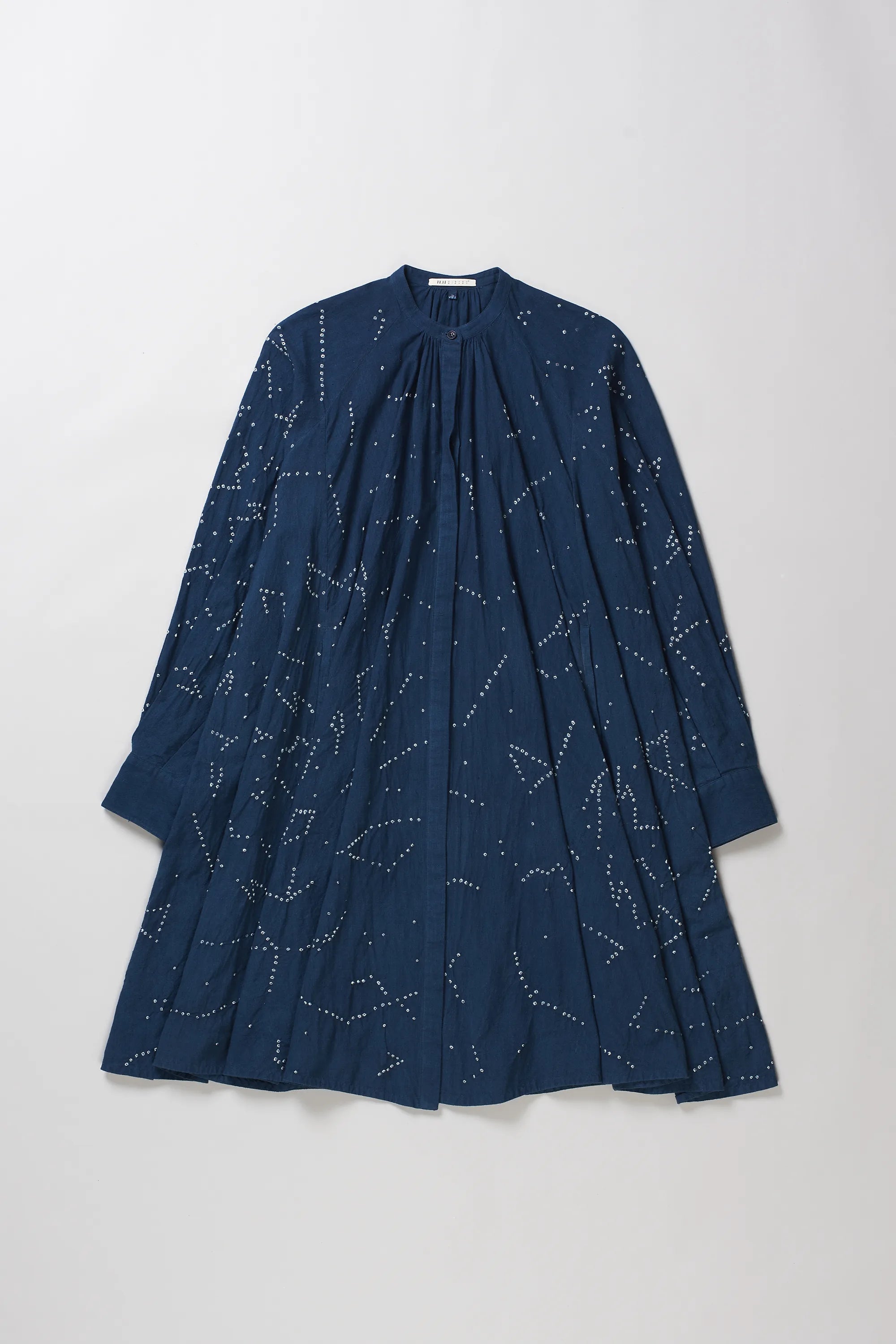 A space blue long-sleeve dress with a gathered, pleated design and bandhani artwork, displayed flat against a grey background.