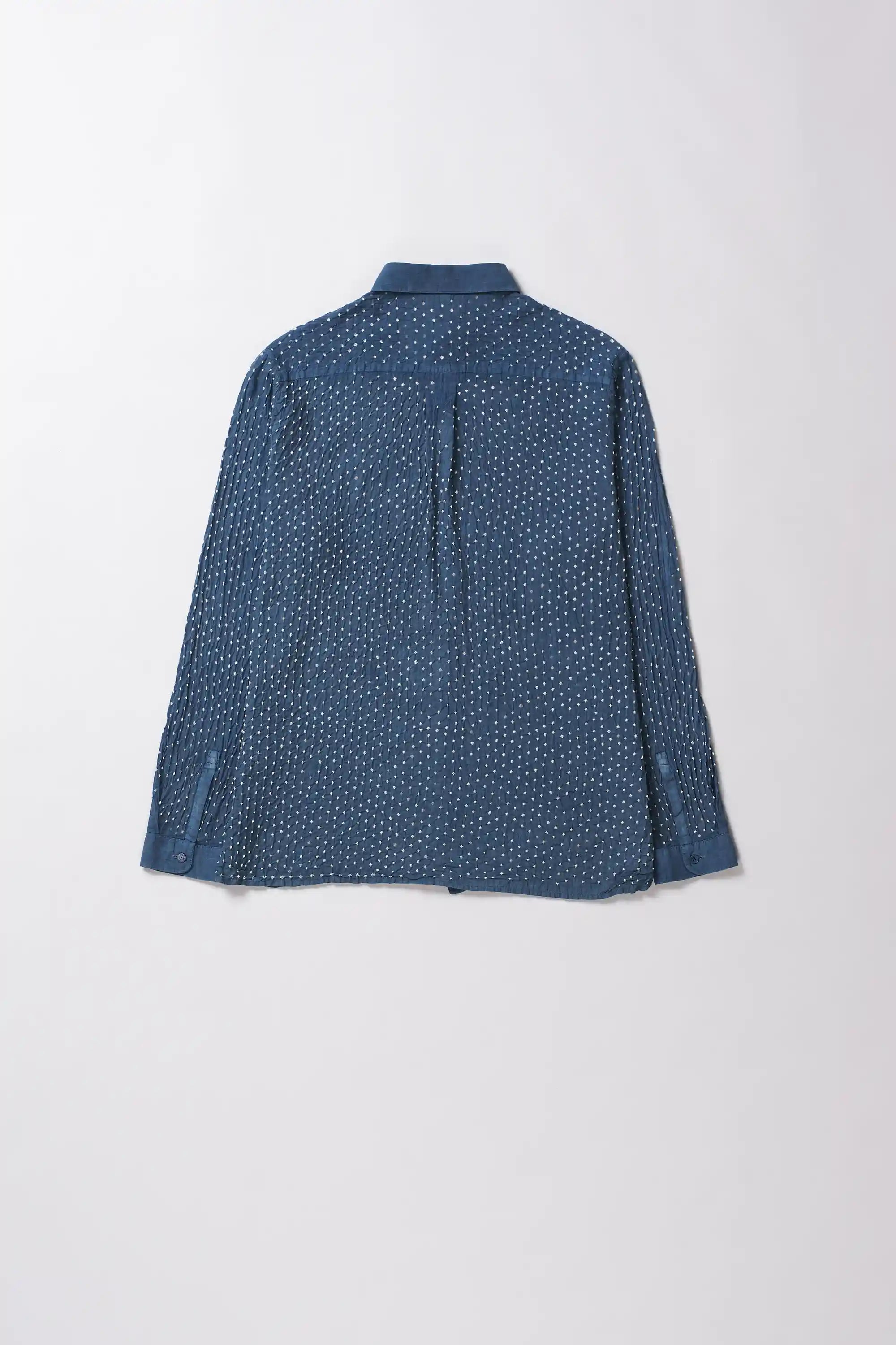 Back shot of long-sleeve button-up shirt in a medium indigo with a dense white micro-dot bandhani pattern, laid flat against a light grey background.