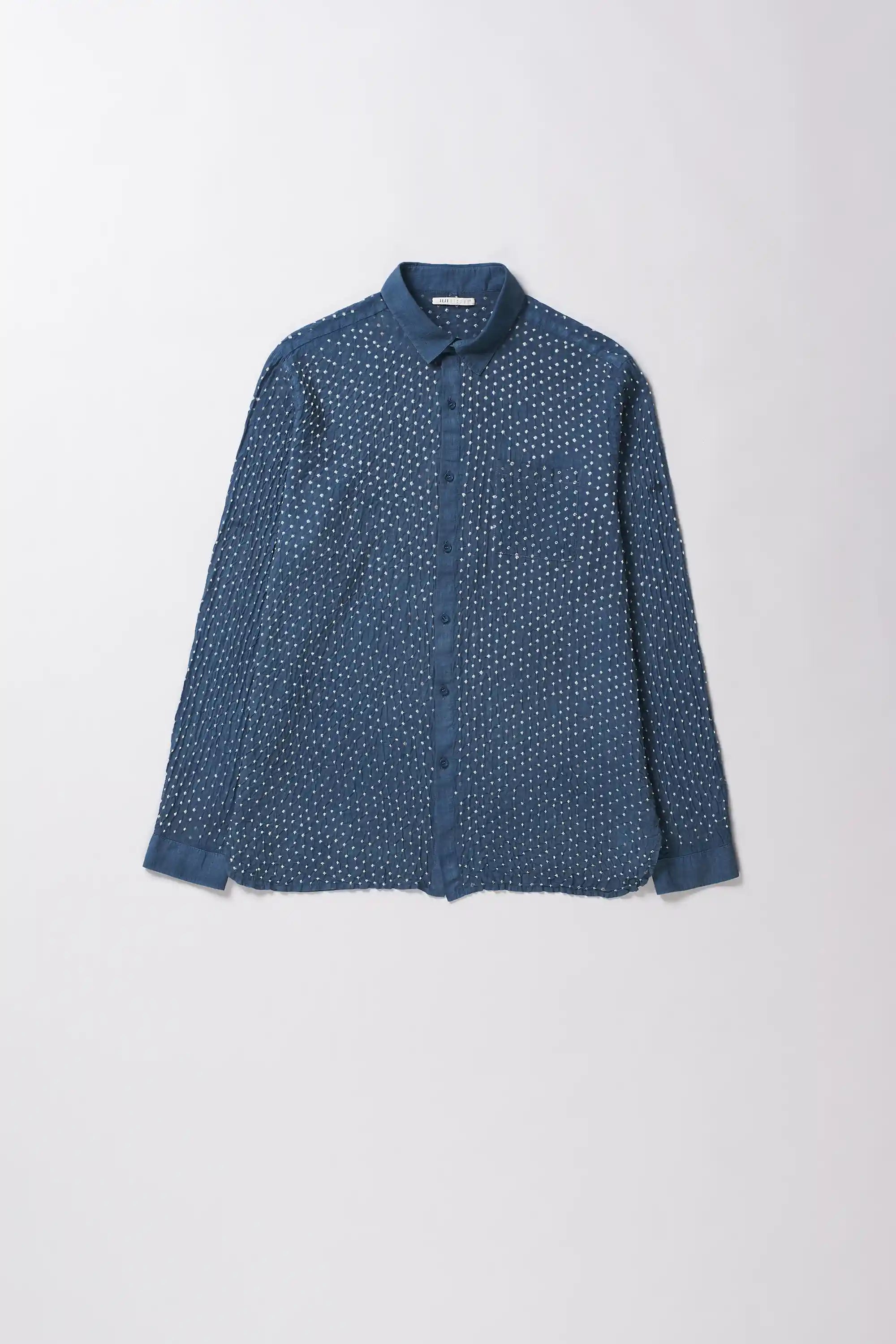 A long-sleeve button-up shirt in a medium indigo with a dense white micro-dot bandhani pattern, laid flat against a light grey background.