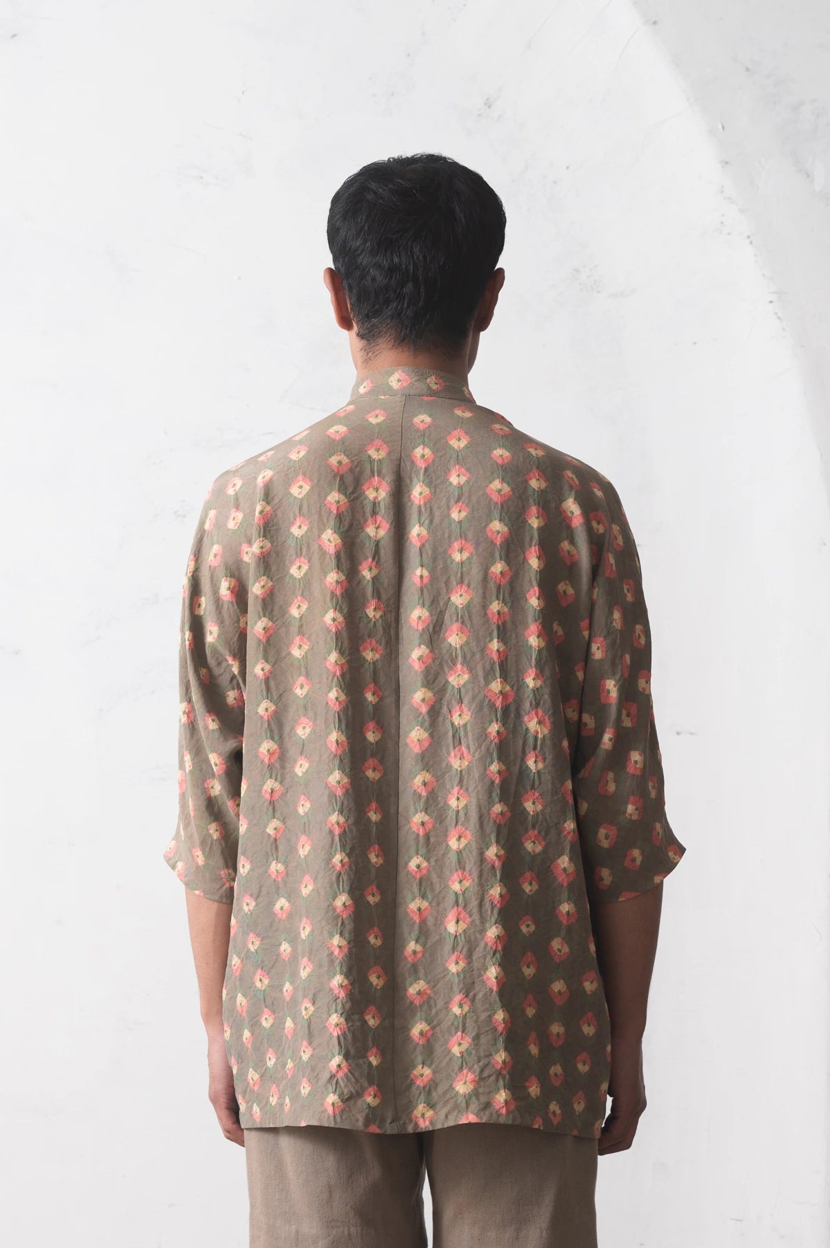 Back shot of a man wearing a bandhani  shirt against a white background