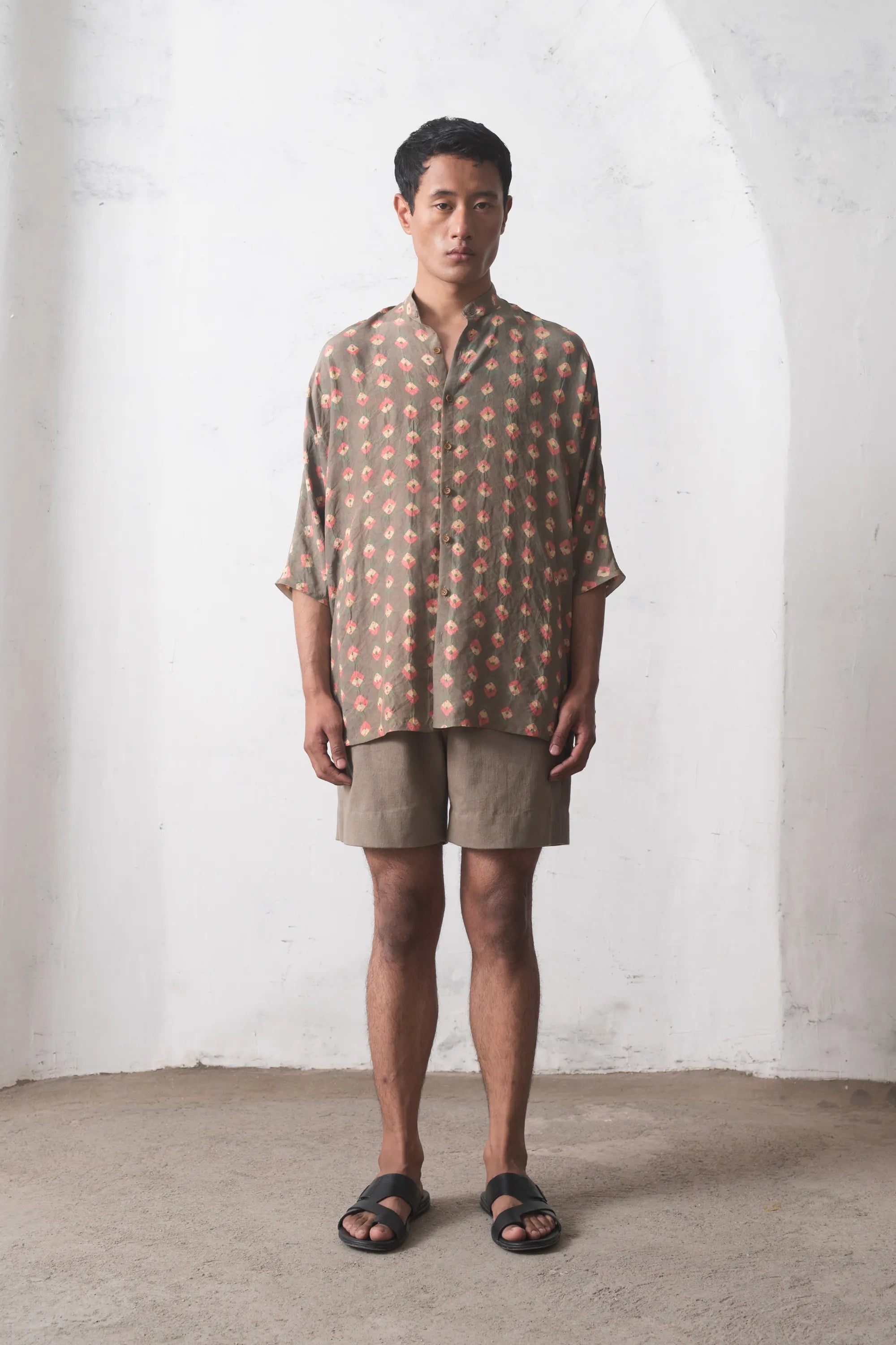 Man wearing a multicolour shirt and beige shorts against a white wall