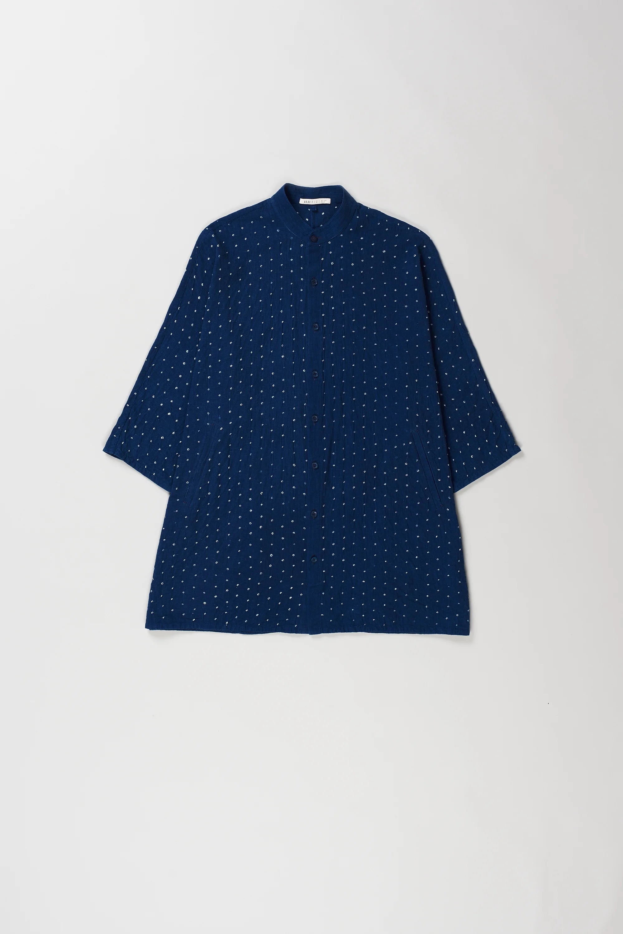 A medium indigo short-sleeve shirt with a bandhani dot pattern, laid flat against a light gray background.