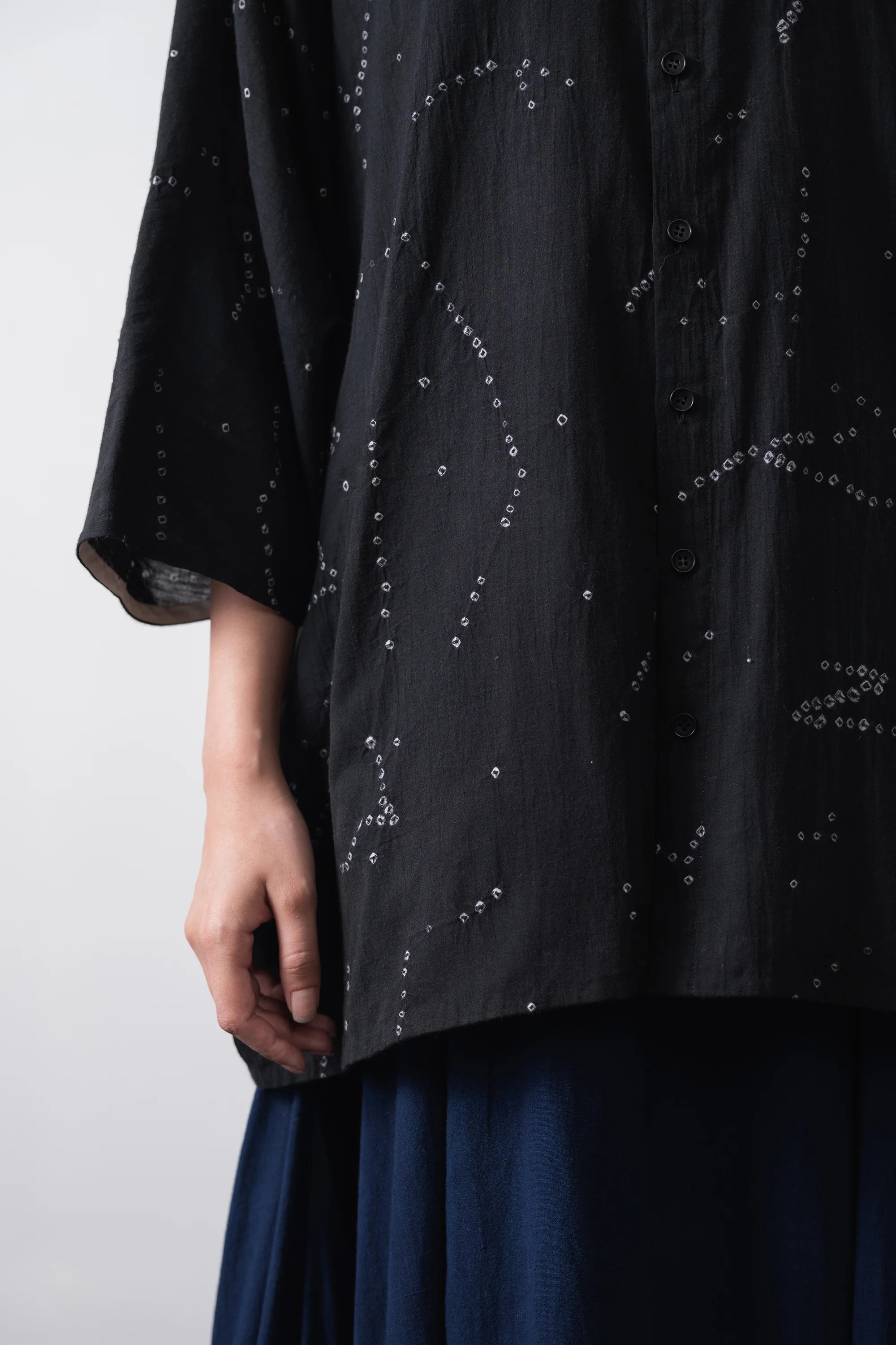 A black short-sleeve button-up shirt with an all-over white line-art constellation pattern bandhani, laid flat against a light grey background.