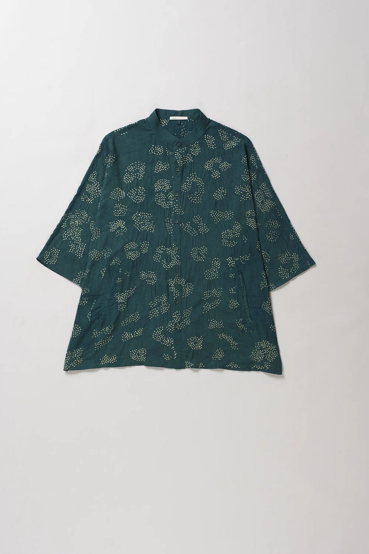 A bottle green short-sleeve shirt with a light beige floral bandhani, laid flat against a grey background.