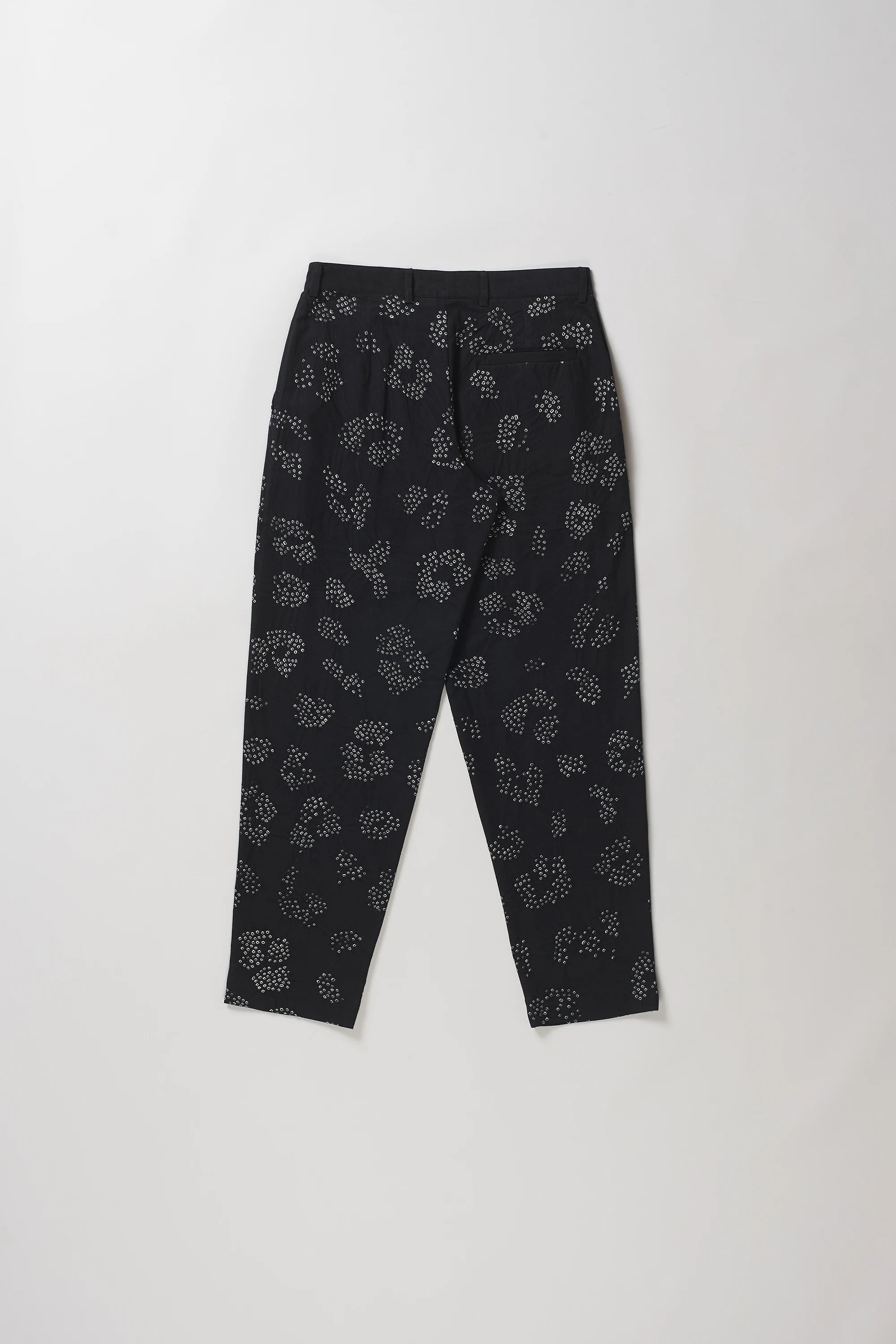 Back shot of black trousers with a white floral bandhani, laid flat against a light grey background.