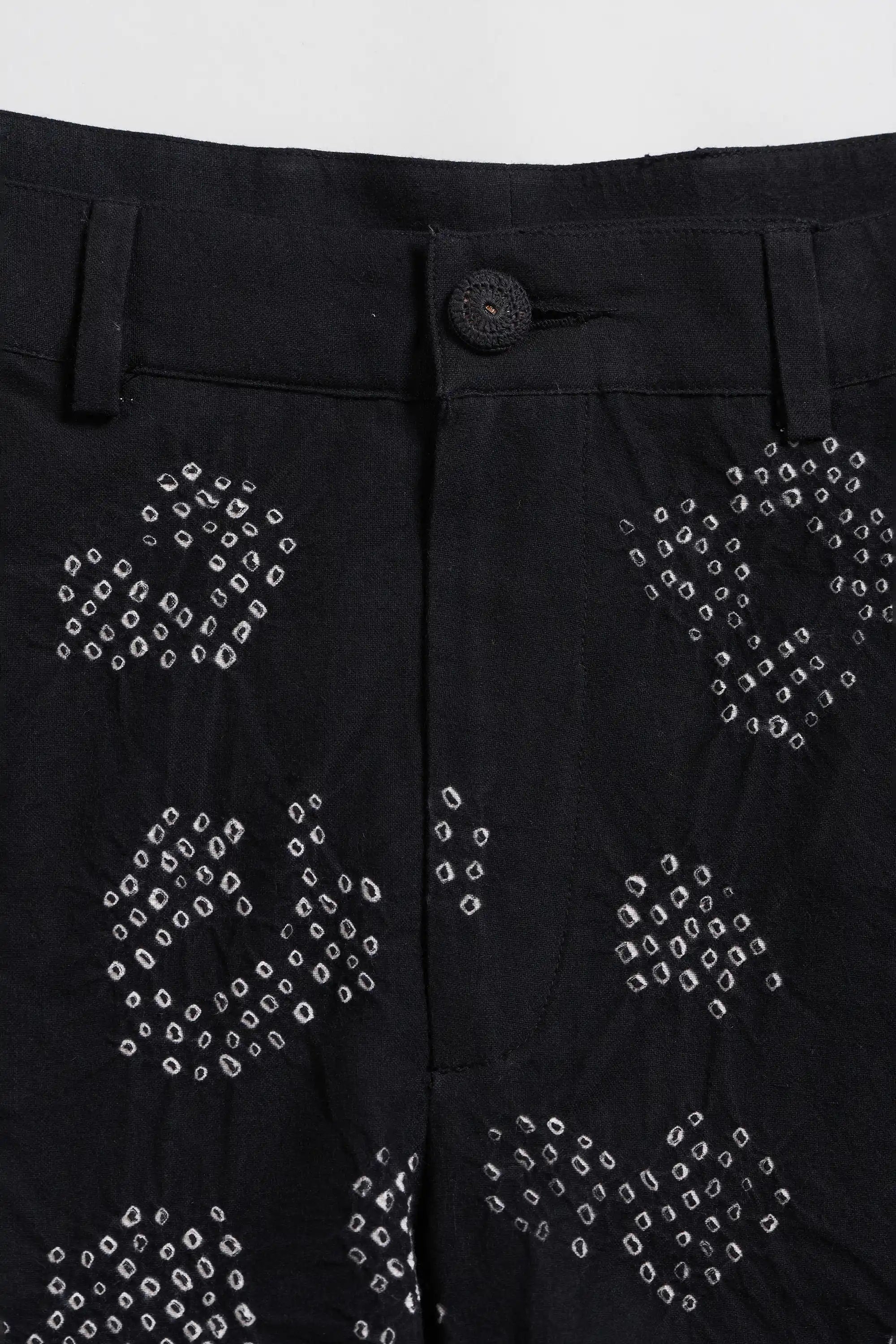 Close-up of black trousers featuring white tie-dye bandhani patterns and a single button closure at the waist.