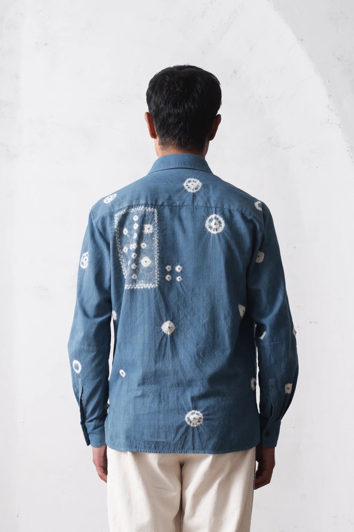 Back shot of a person wearing a blue cotton shirt with shibori on a light grey background