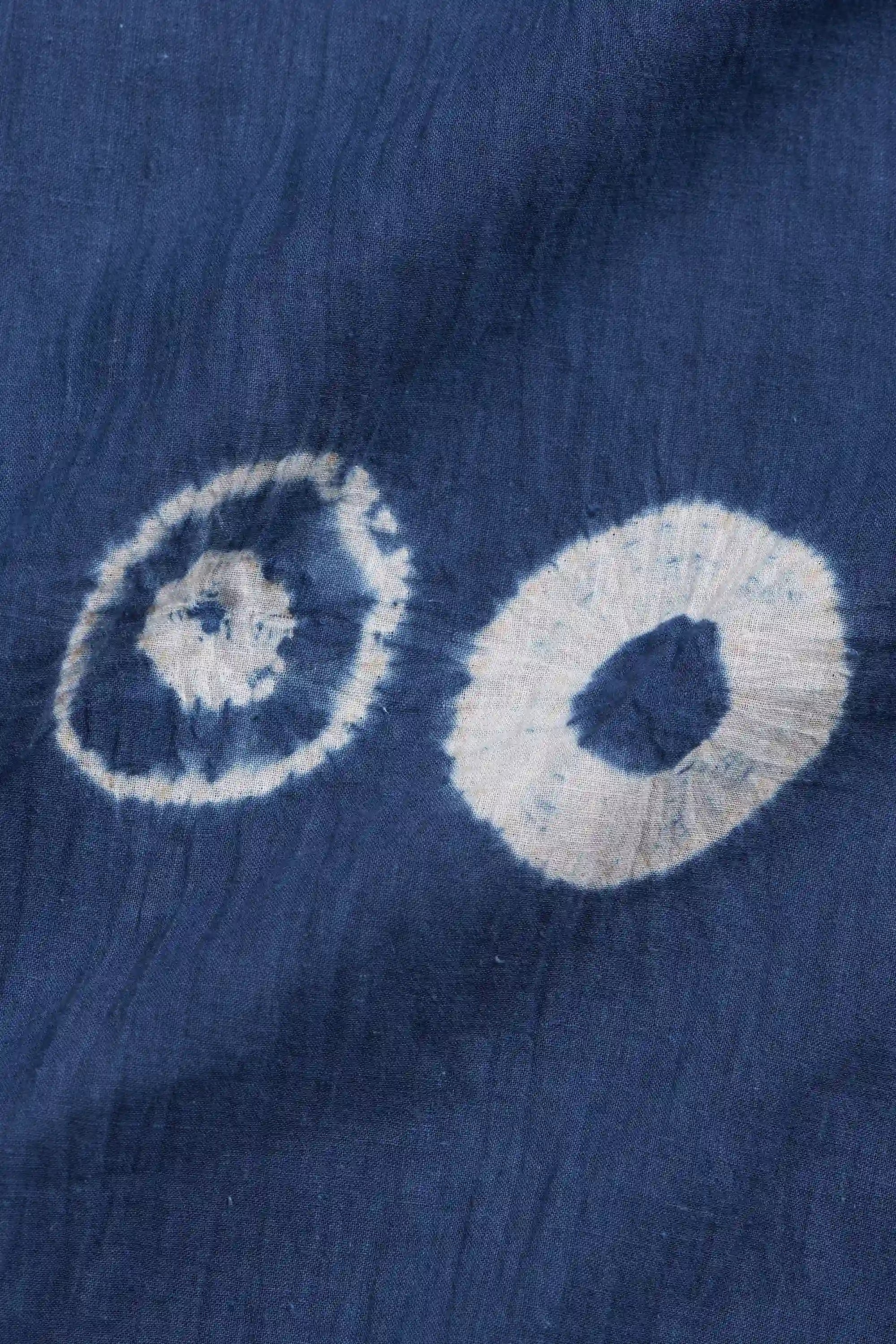 A close-up of medium indigo fabric with two white tie-dye rings, showing a textured