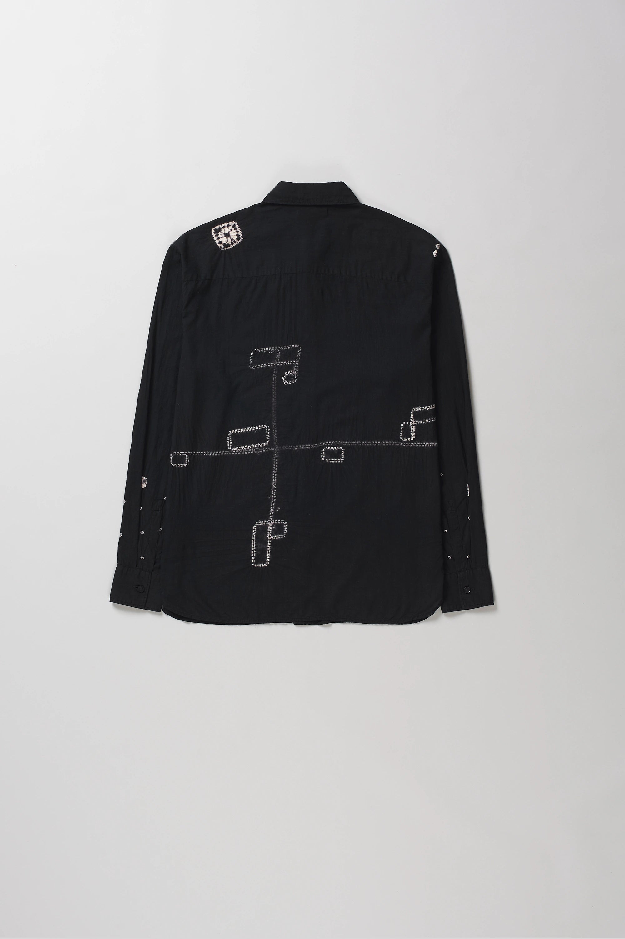 Back shot of shirt with white geometric line-art shibori, from the back against a light gray background.