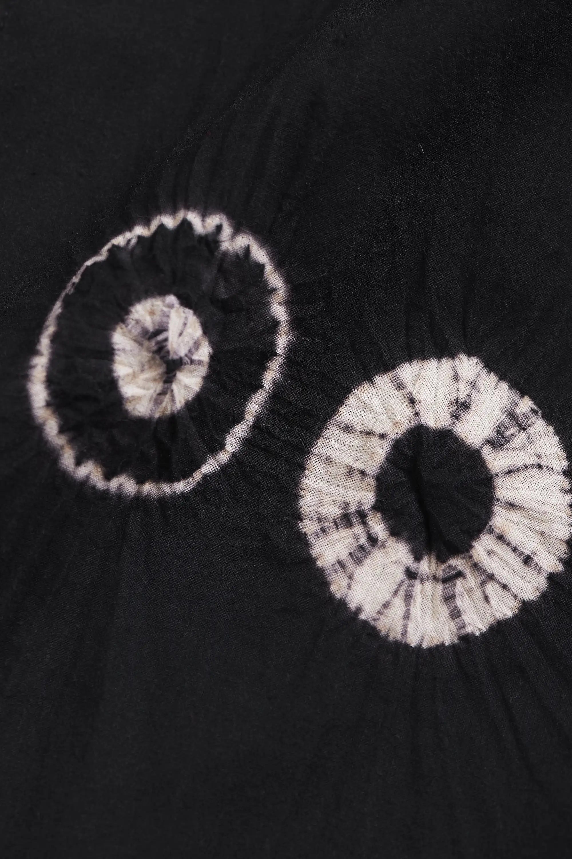 Black fabric closeup with two circular tie-dye shibori patterns in white and gray.