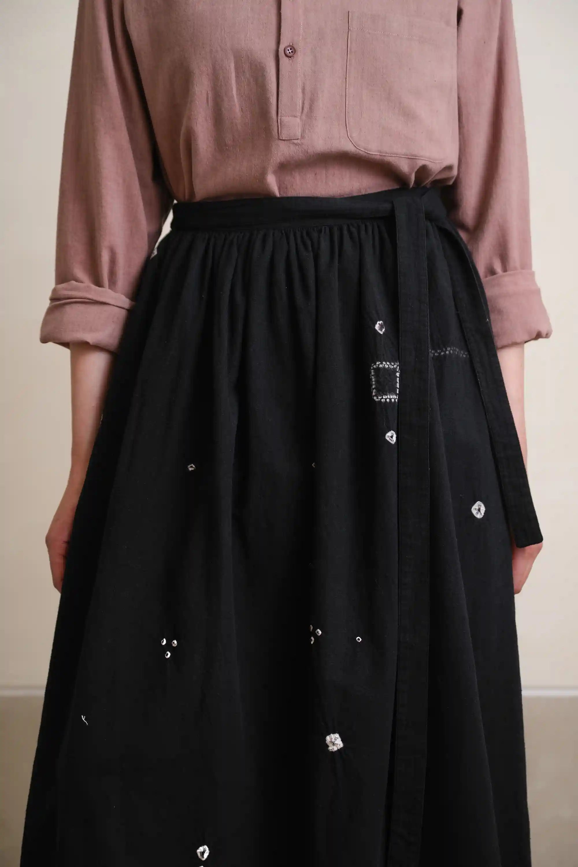 Person wearing a black skirt with white buttons and a pink shirt against a neutral background