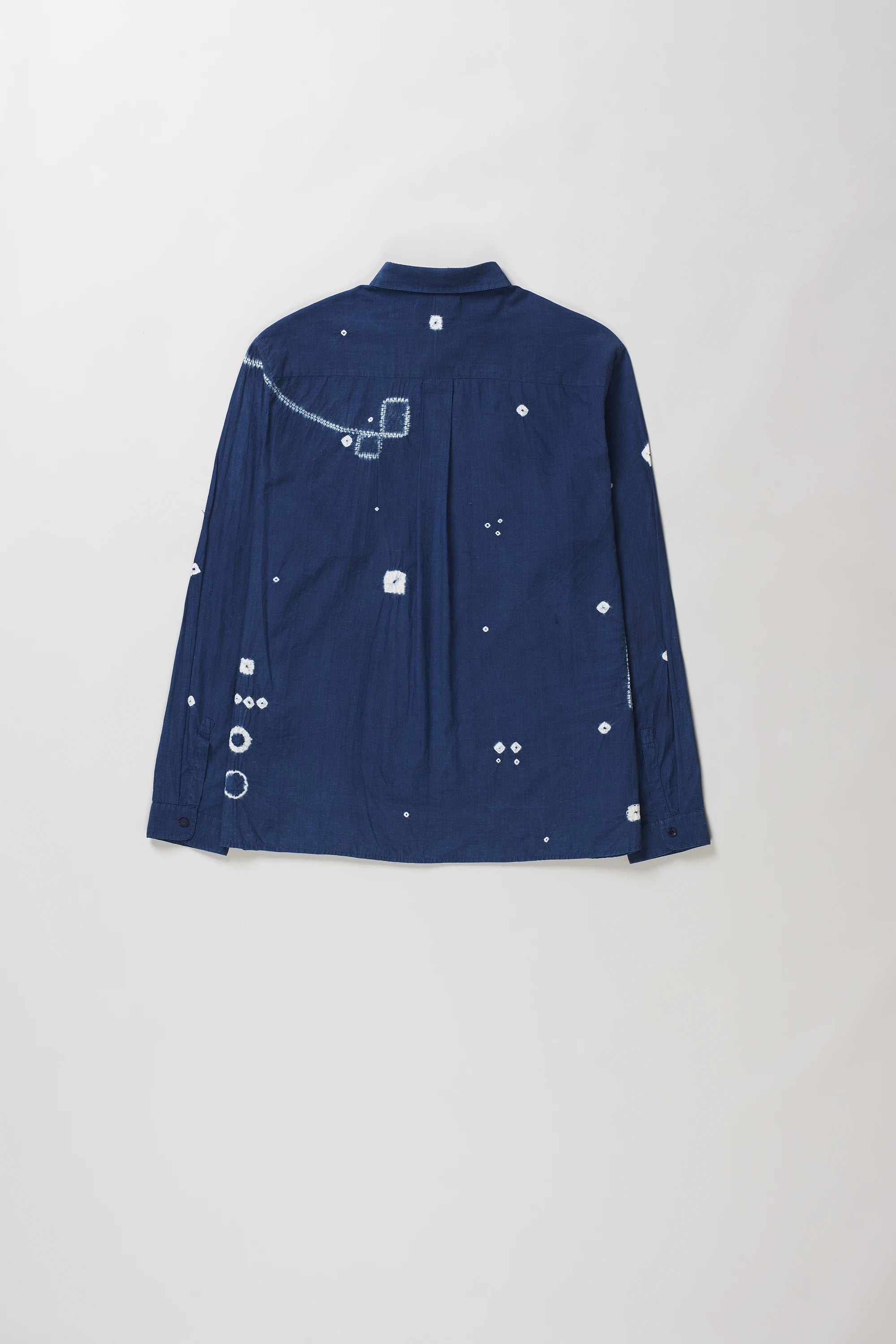 Back shot of medium indigo long-sleeve button-up shirt with white shibori details, laid flat against a light grey background.