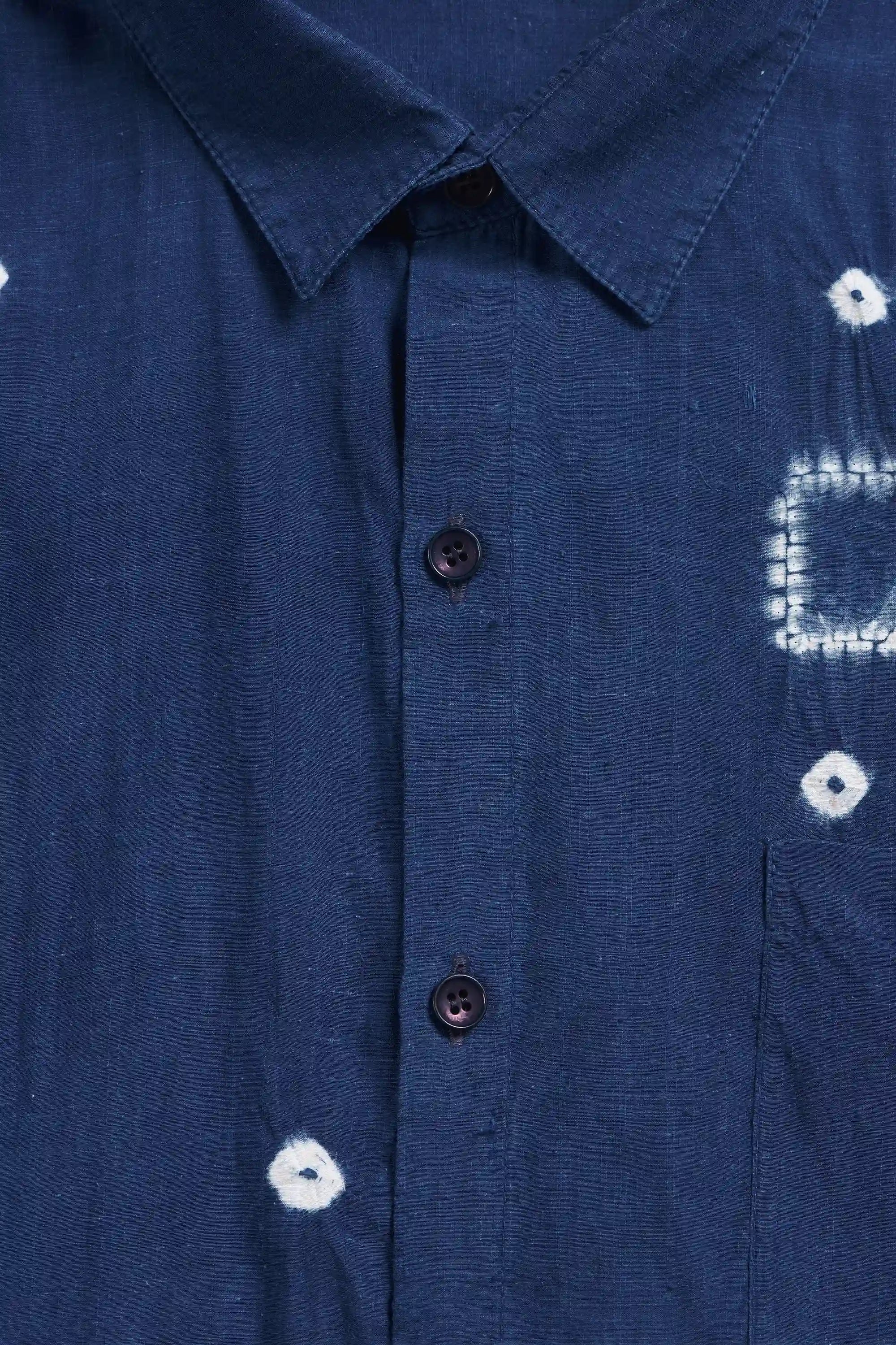 Close-up of a indigo button-down shirt with white tie-dye style patterns and dark buttons.