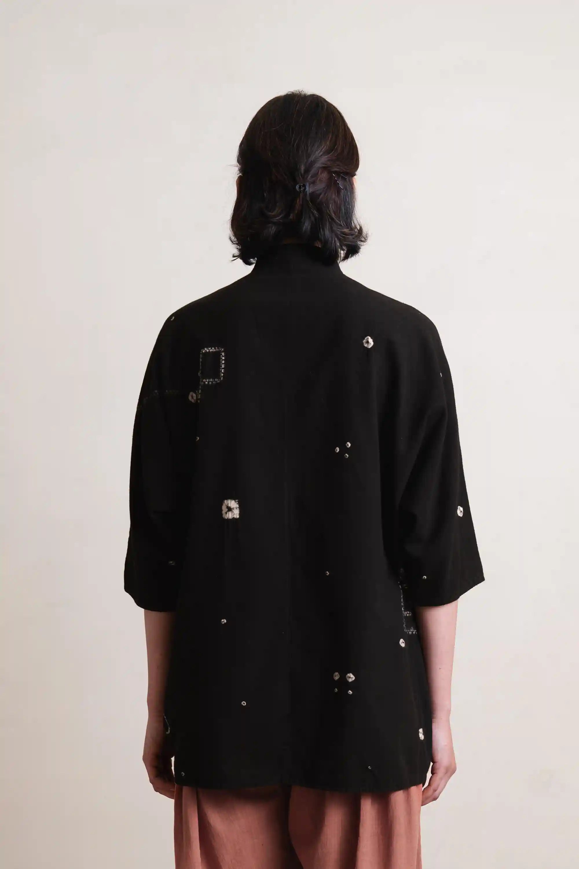 Person wearing a black jacket with decorative buttons on a plain background