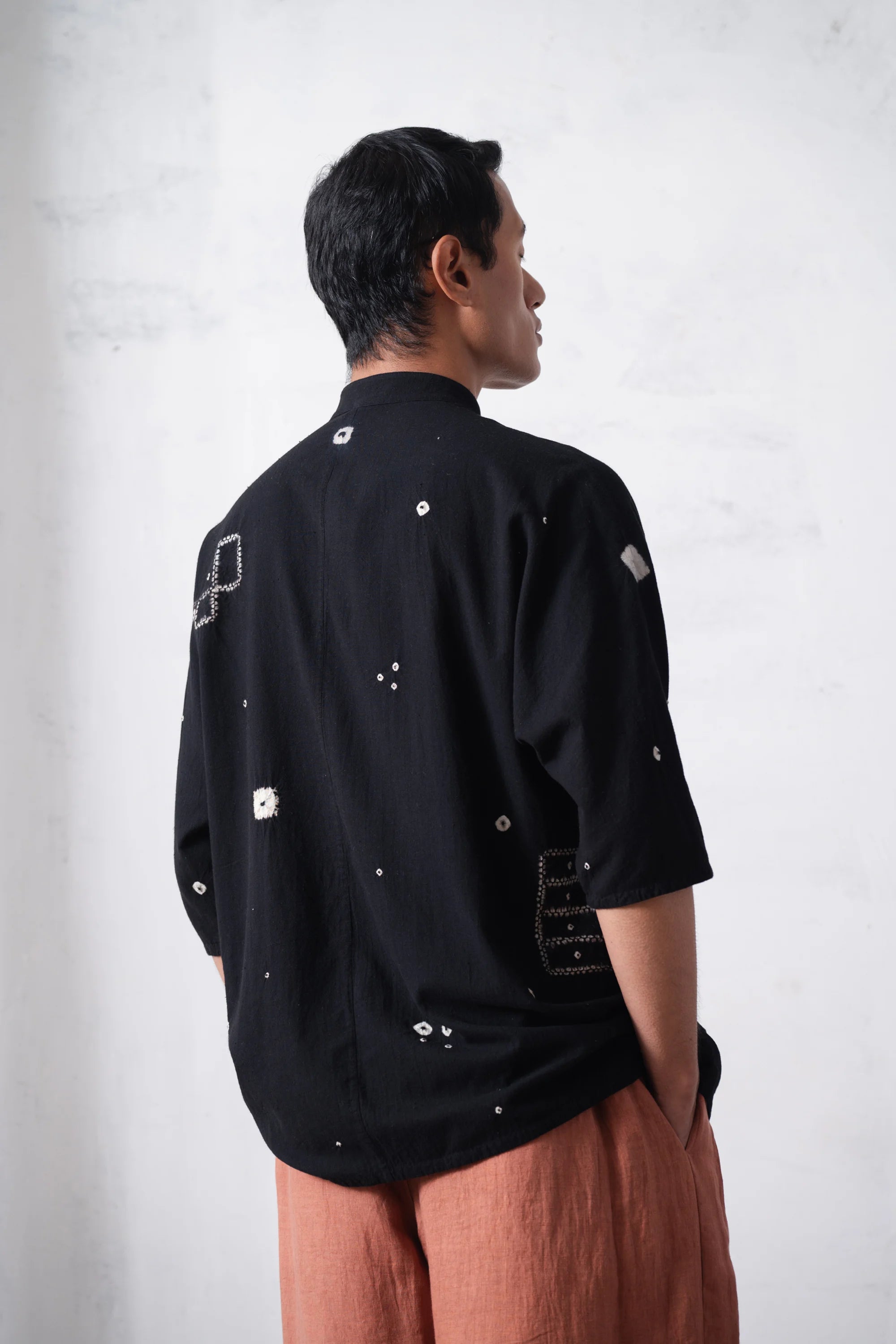 back shot of a man wearing a black shirt with shibori work on a light grey background