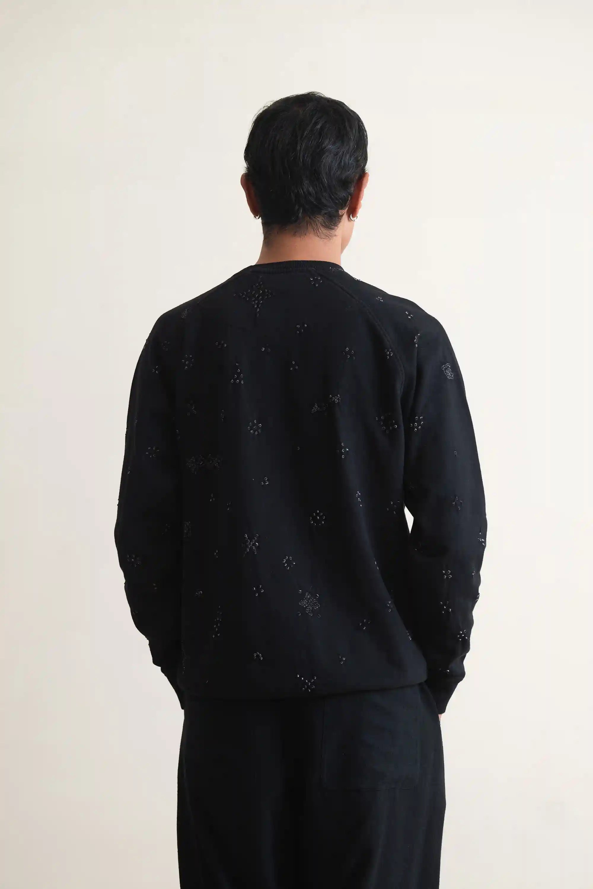 Person wearing a black sweater with small bandhani on a plain background