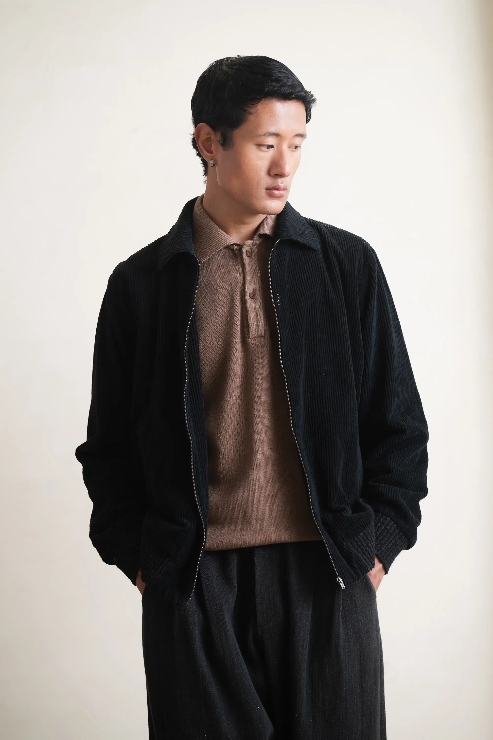 Man wearing a black jacket over a brown shirt against a light grey background