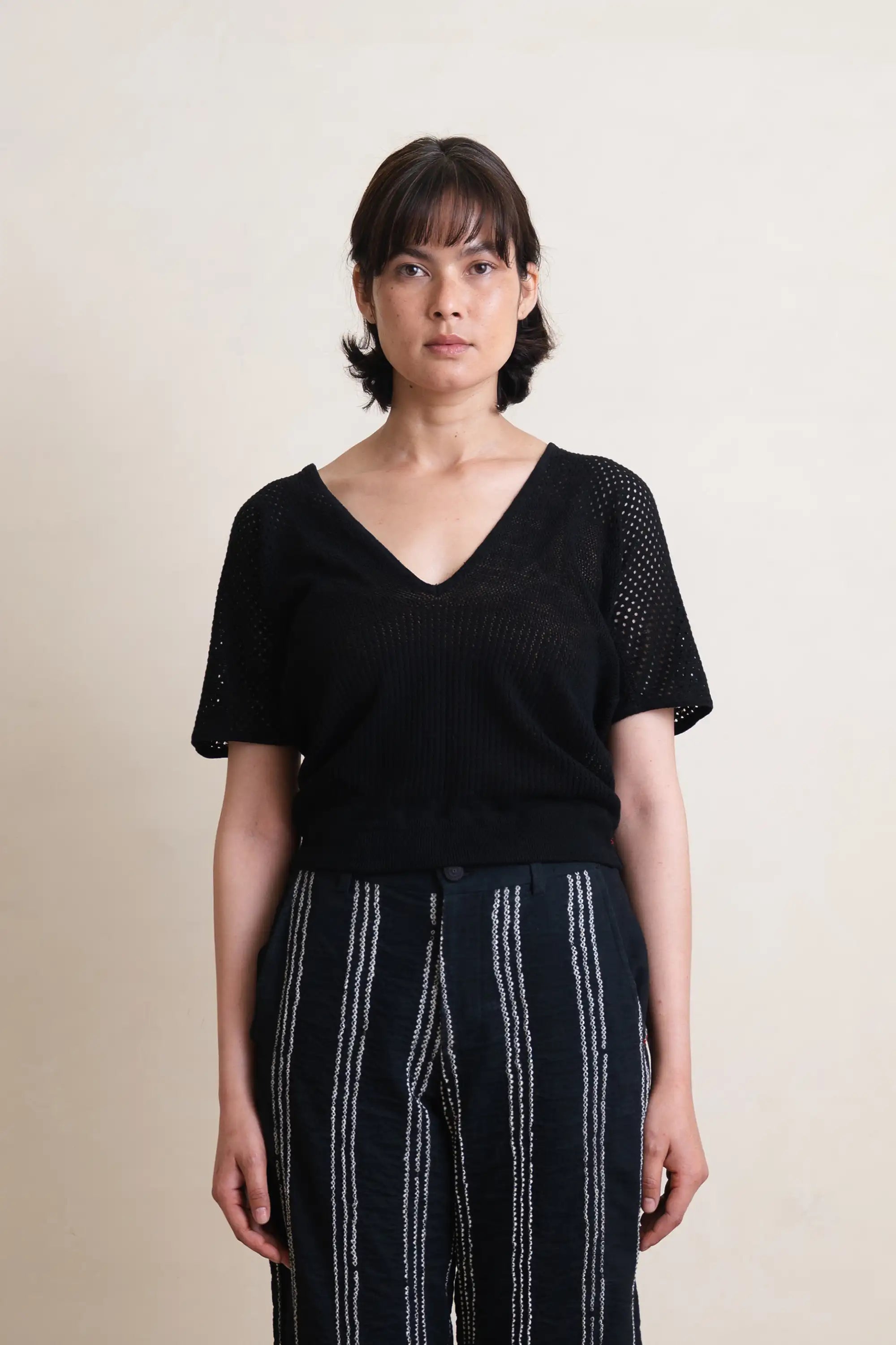 Woman wearing a black top and dark pants with white stripes on a beige background