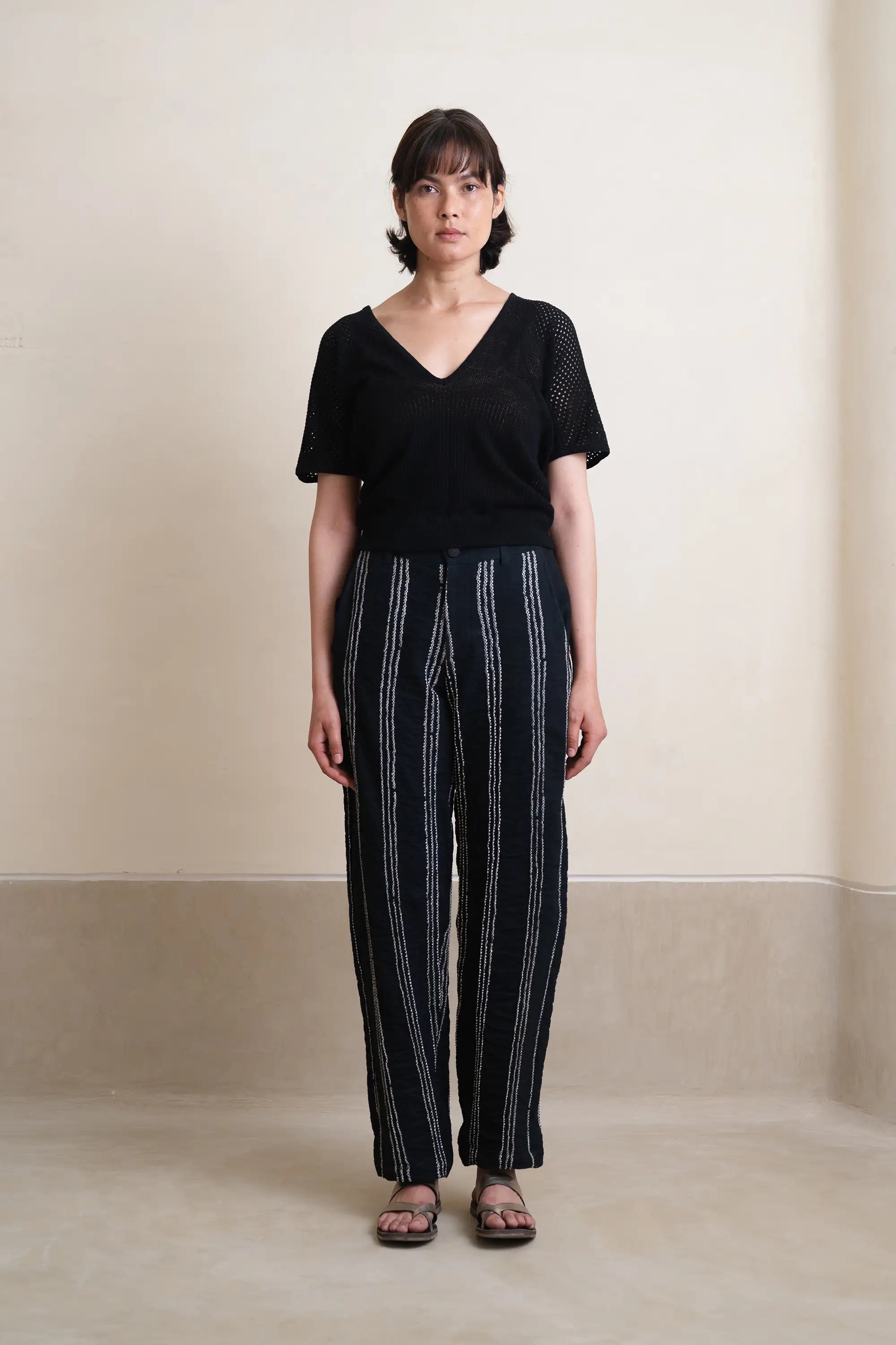 Person wearing a black top and striped pants against a plain background