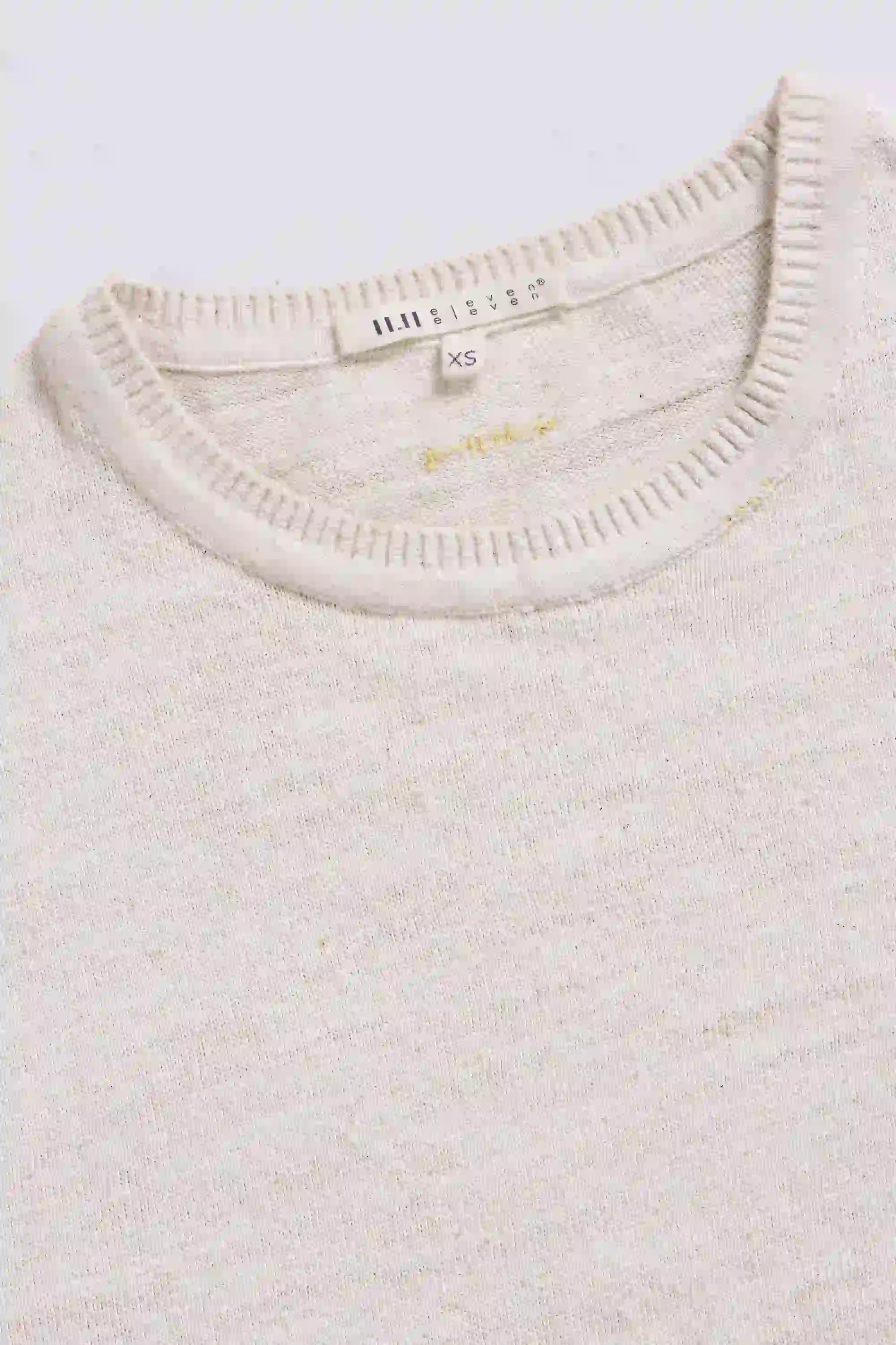 Close-up of a ecru t-shirt with a brand label on a grey background
