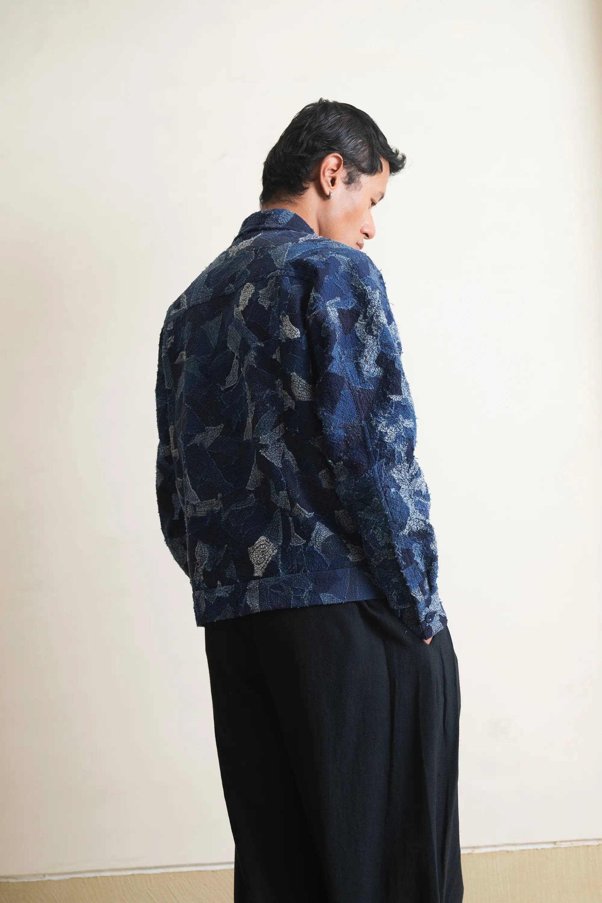 A side shot of a person wearing a blue patchwork jacket against a light grey background