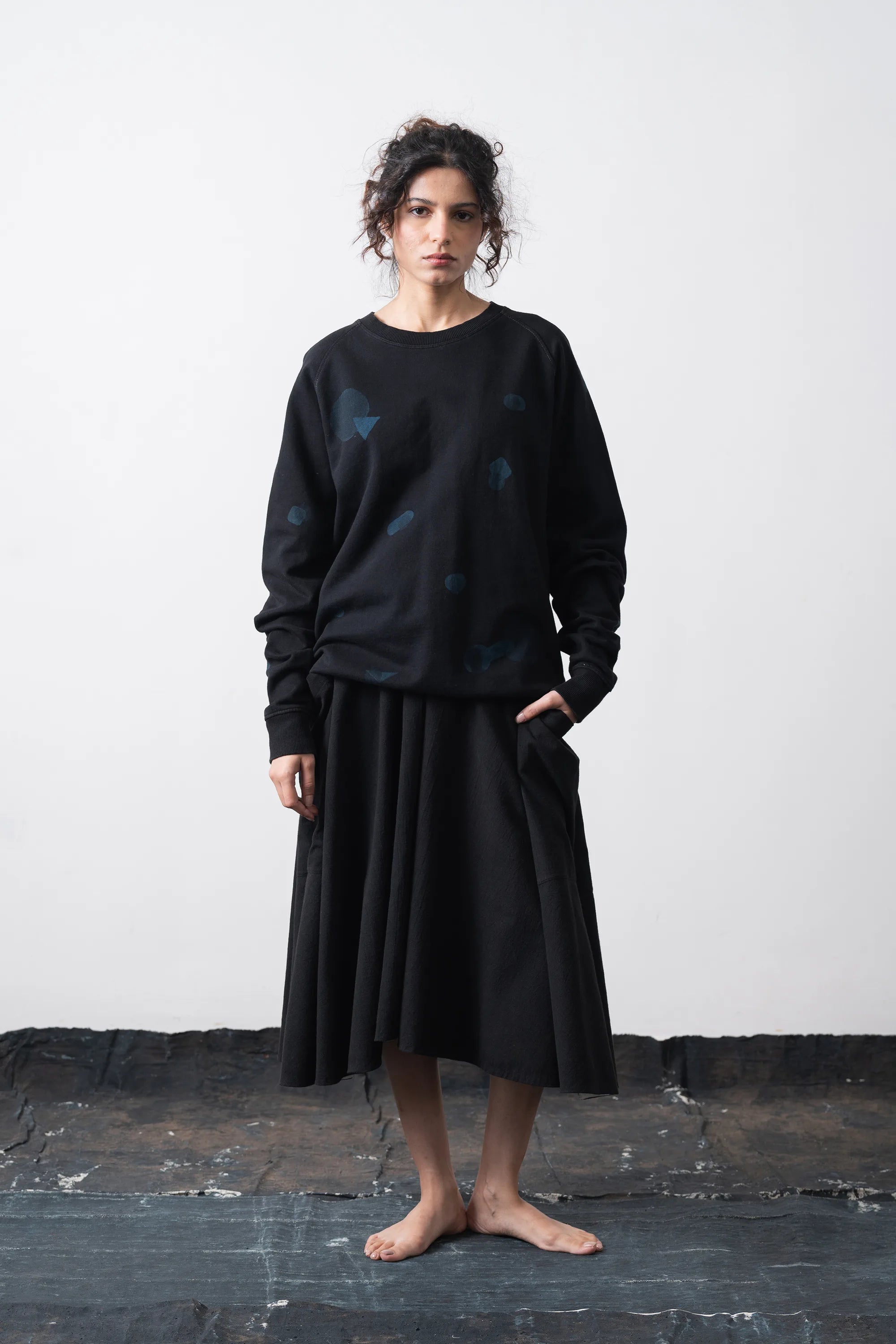 A woman model a black crewneck sweatshirt with subtle blue geometric patterns, paired with a black sweatshirt, against a plain light grey background.