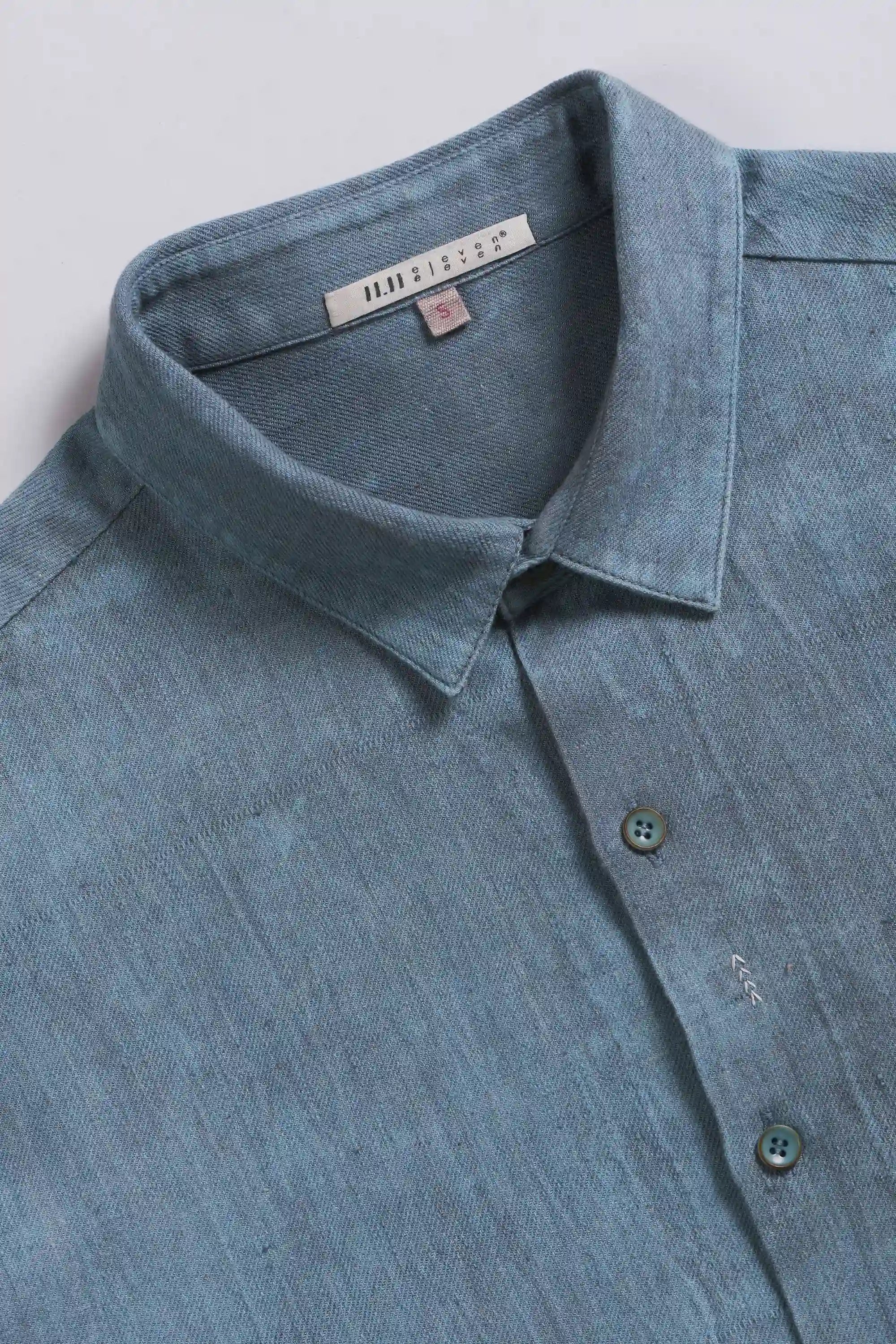 Close-up of a blue shirt collar with a brand label on a light grey background